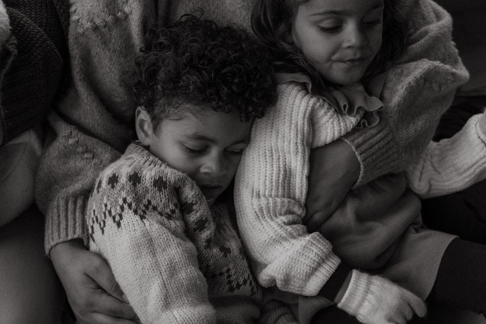 A tender black and white photograph capturing children cuddling in cozy sweaters.