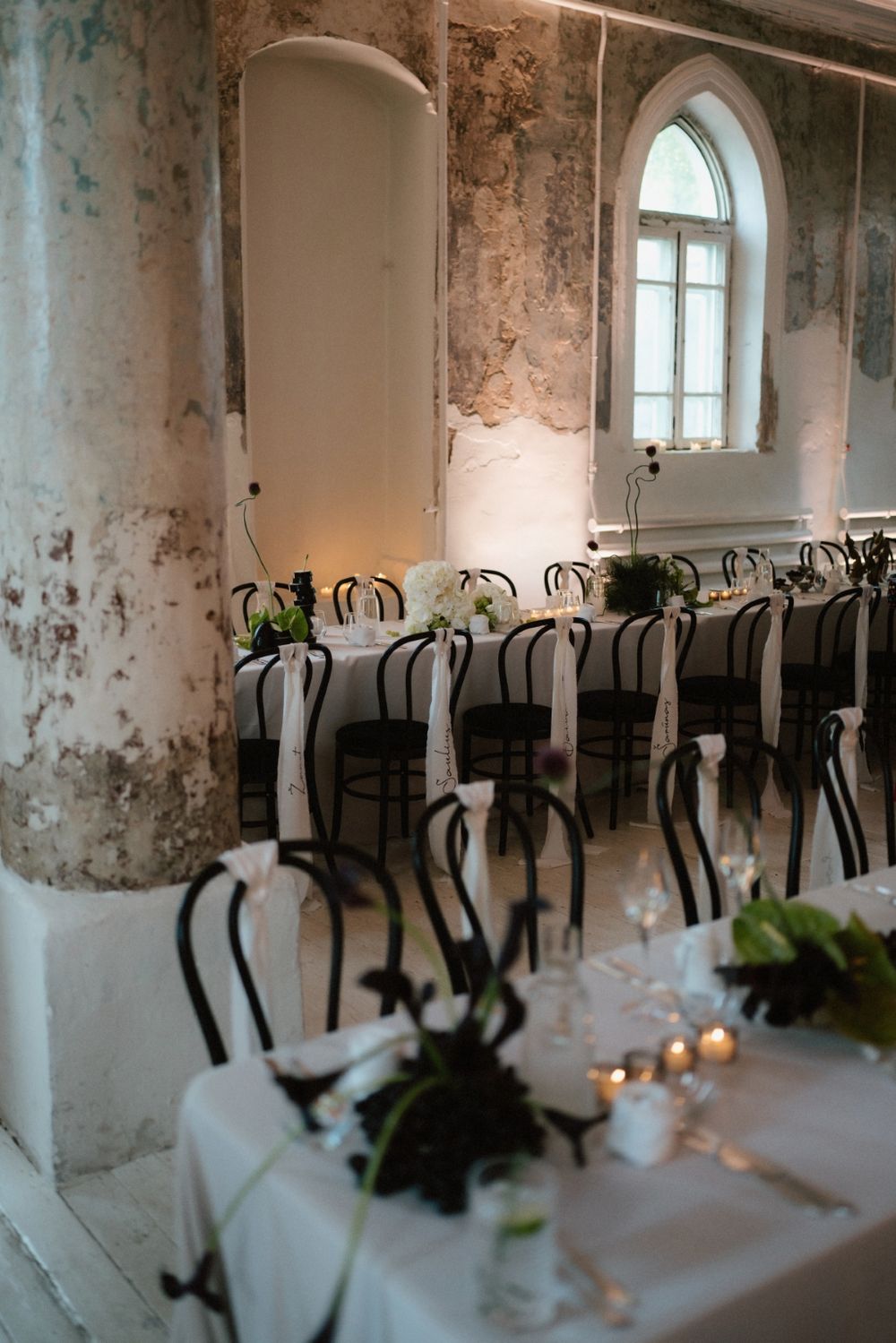 Elegant dining room setup with bentwood chairs and white tablecloths under arched windows.