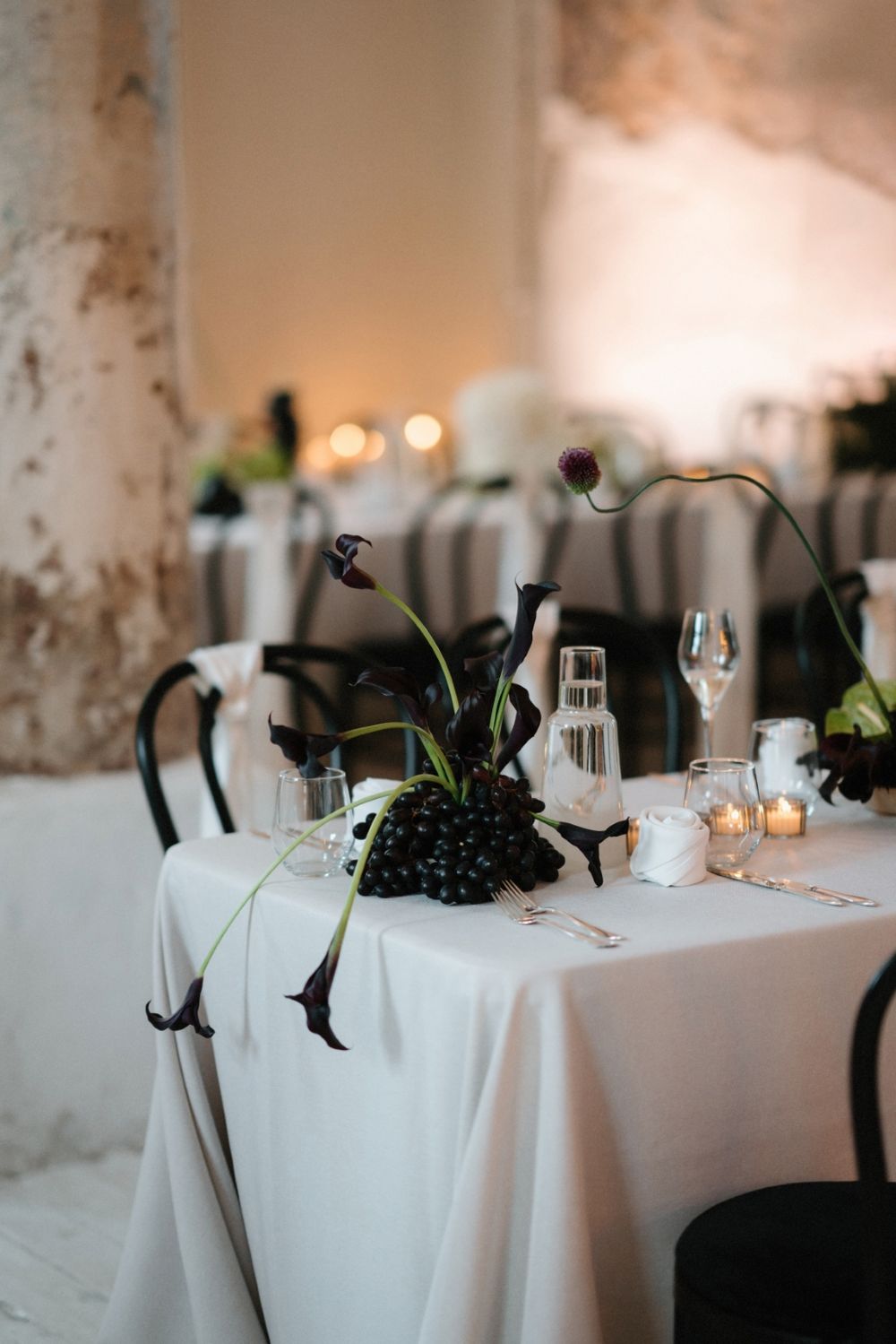 Wedding table setting with dark floral centerpiece, candles and white linens.