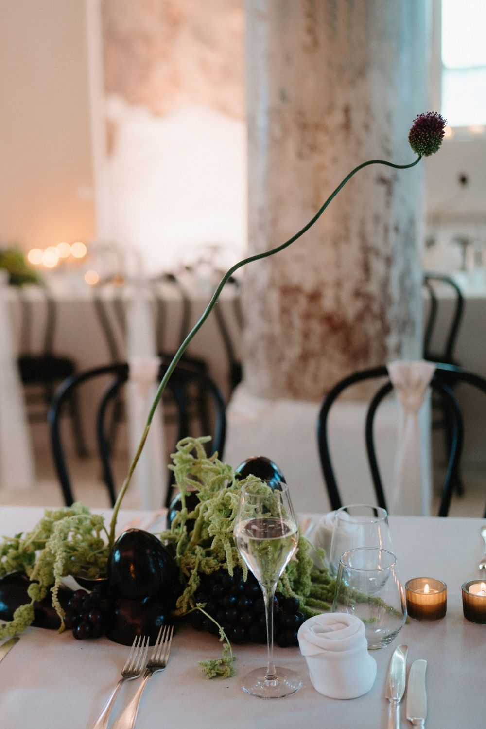Modern table setting with dramatic curved stem flower arrangement and wine glasses.