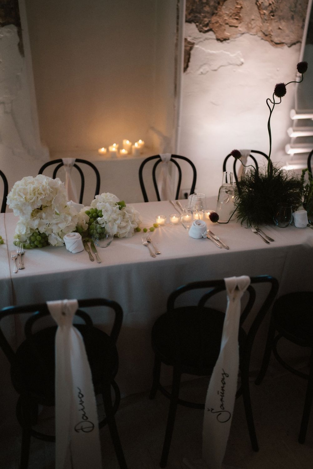 Romantic dining setup with white chair sashes and tealight candles creating soft ambiance.