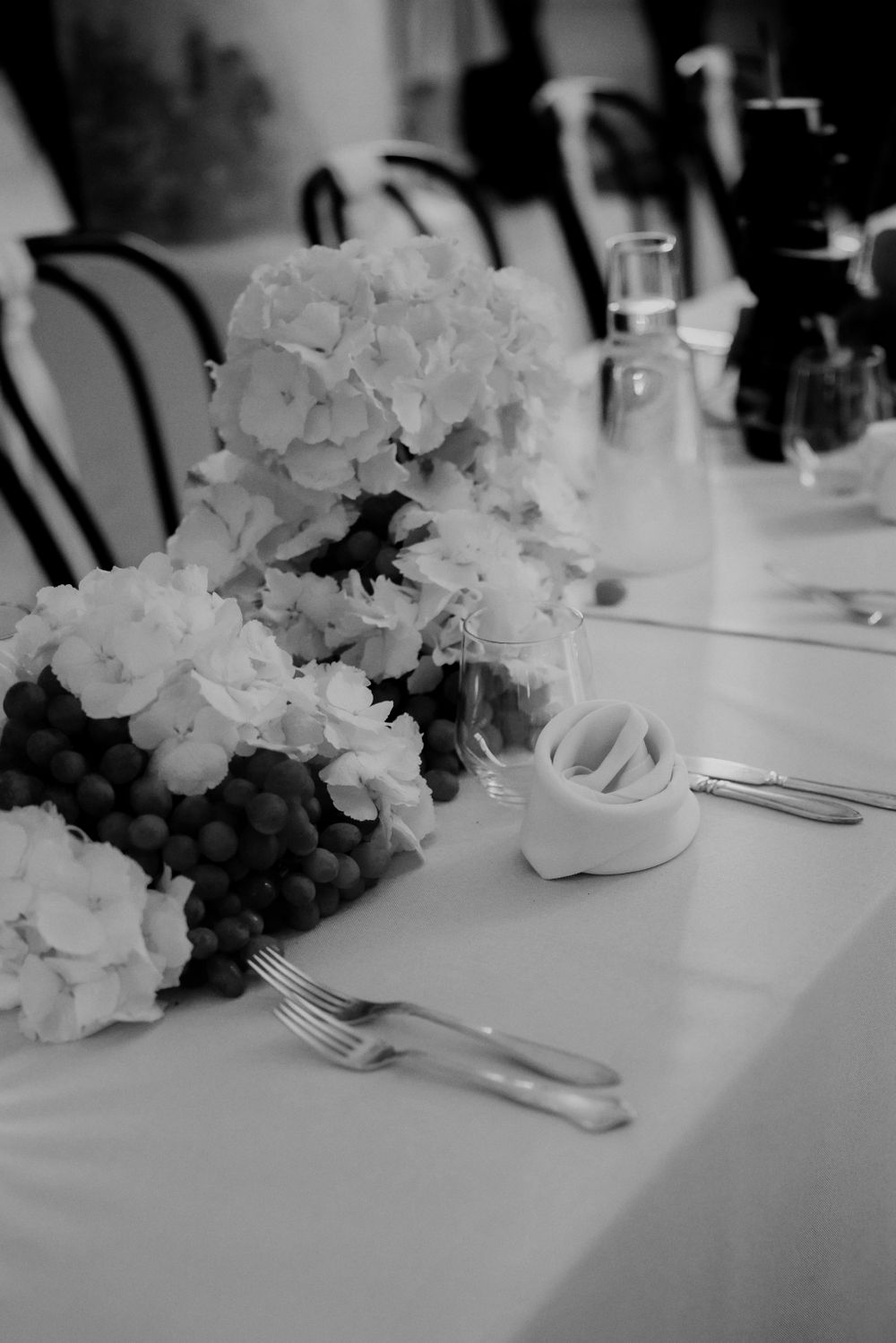 Black and white photo of hydrangea centerpiece with table settings and glassware.
