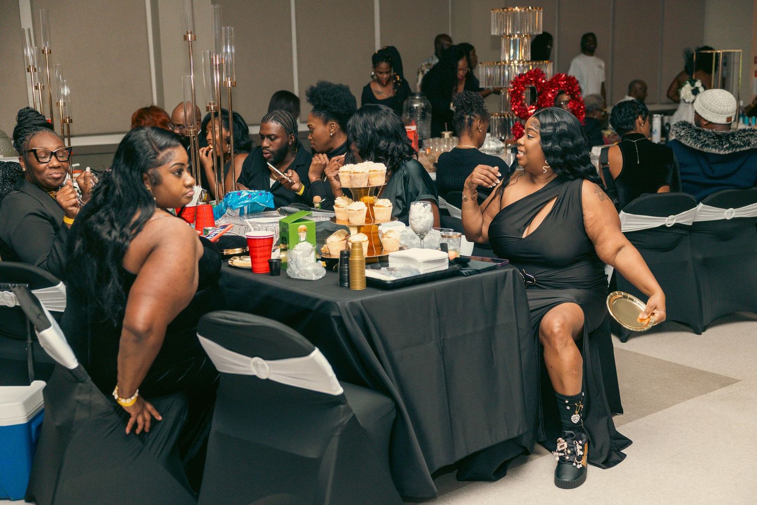 Guests enjoy conversation and refreshments at tables during a black and gold themed event.