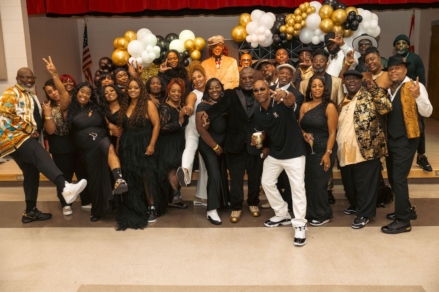 Large group of elegantly dressed guests posing together at a black and gold themed celebration event.