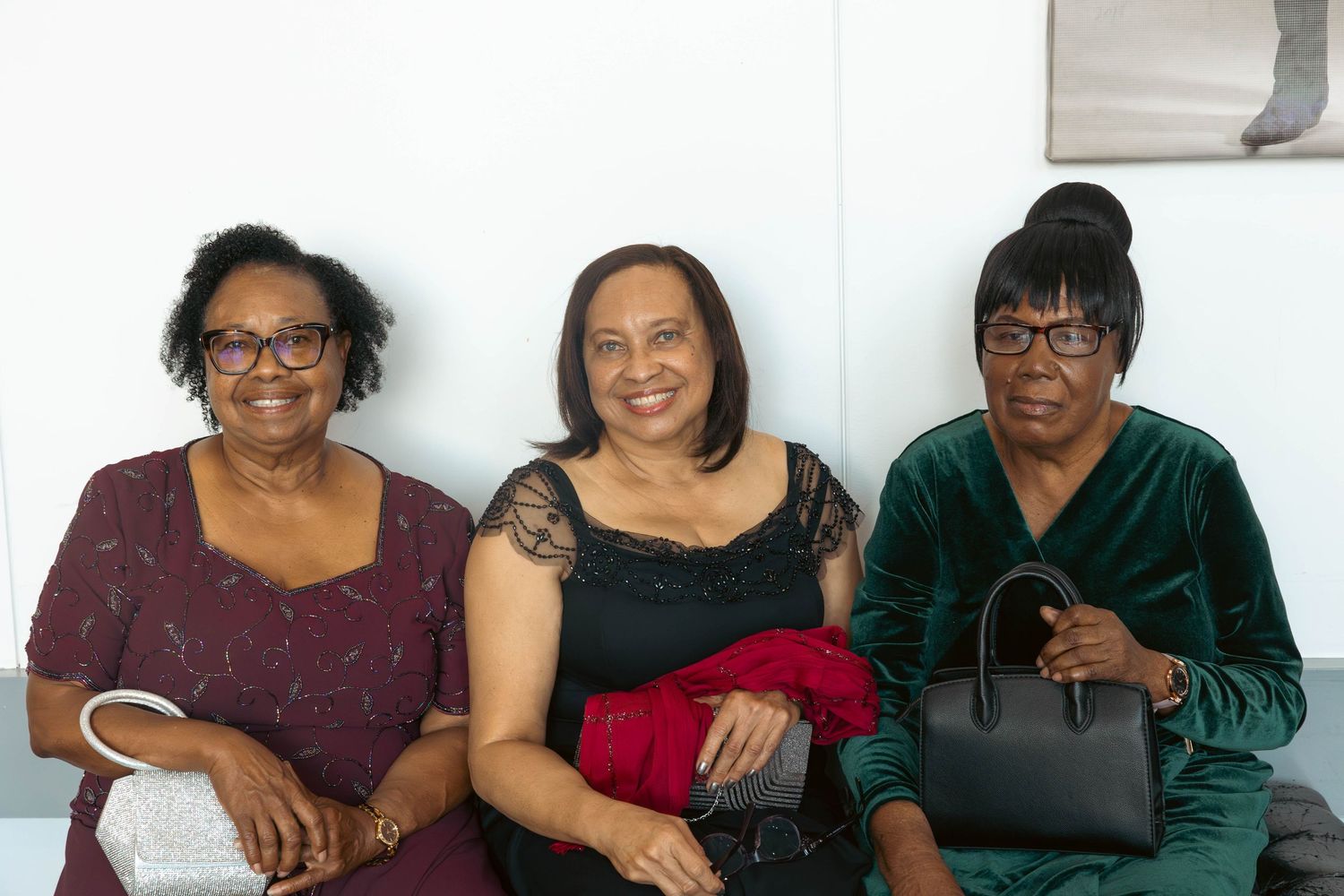 Three smiling women in formal evening wear seated together at a special occasion event.