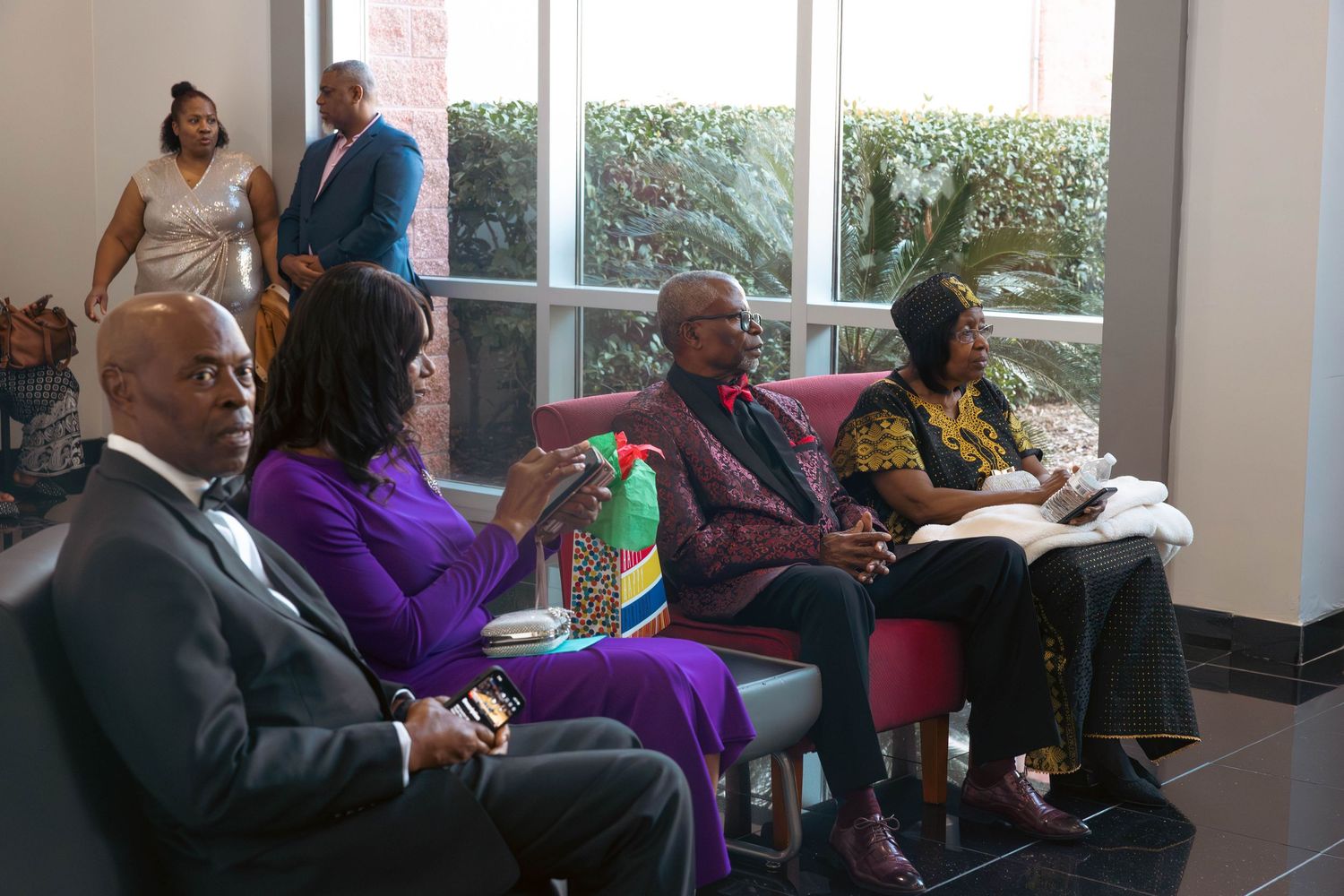 Formally dressed guests seated and socializing in a bright lobby area during a special event.