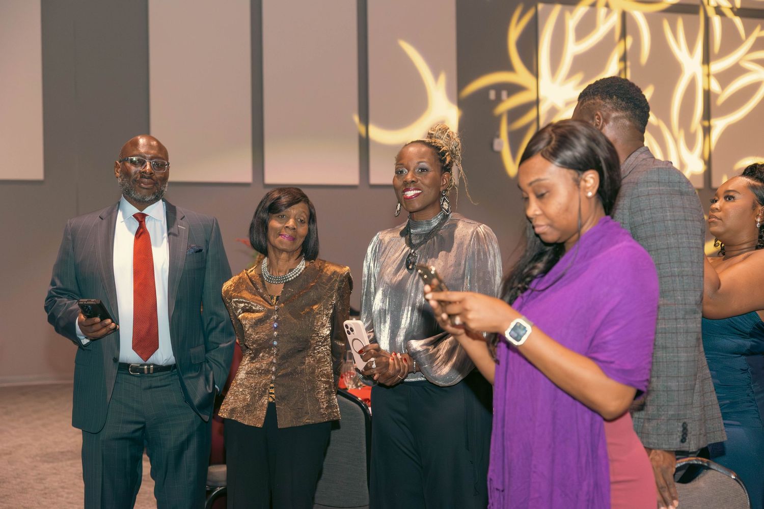 Group of elegantly dressed guests socializing under decorative golden lighting at a formal evening event.
