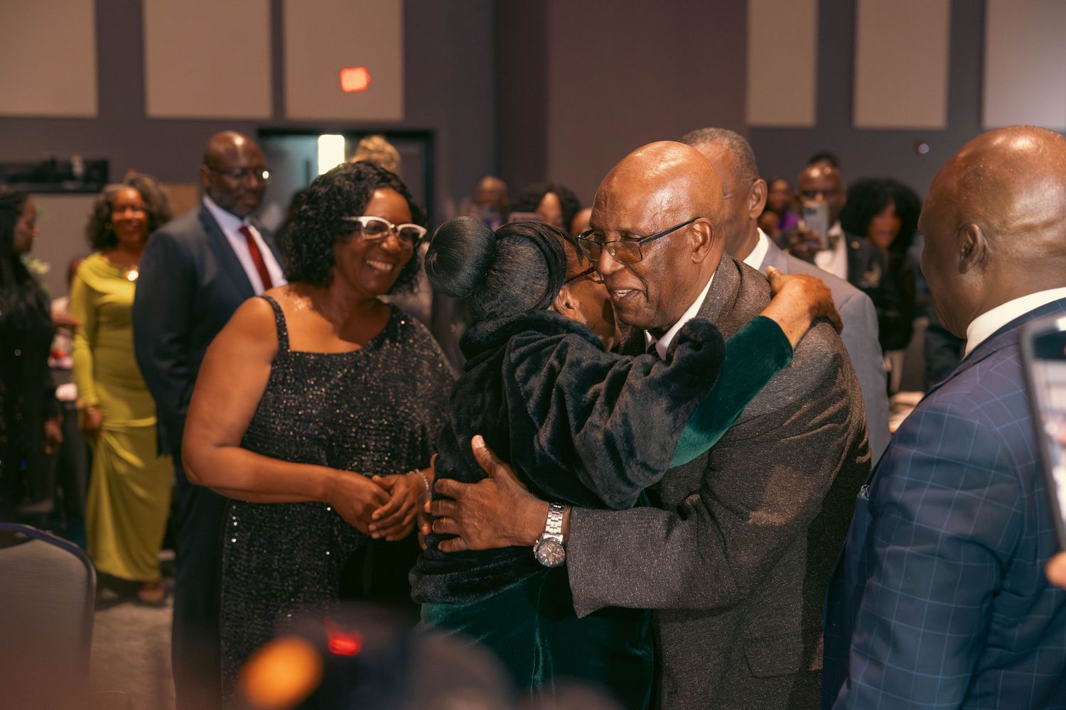 Elegantly dressed guests socialize and embrace at a formal gala event.