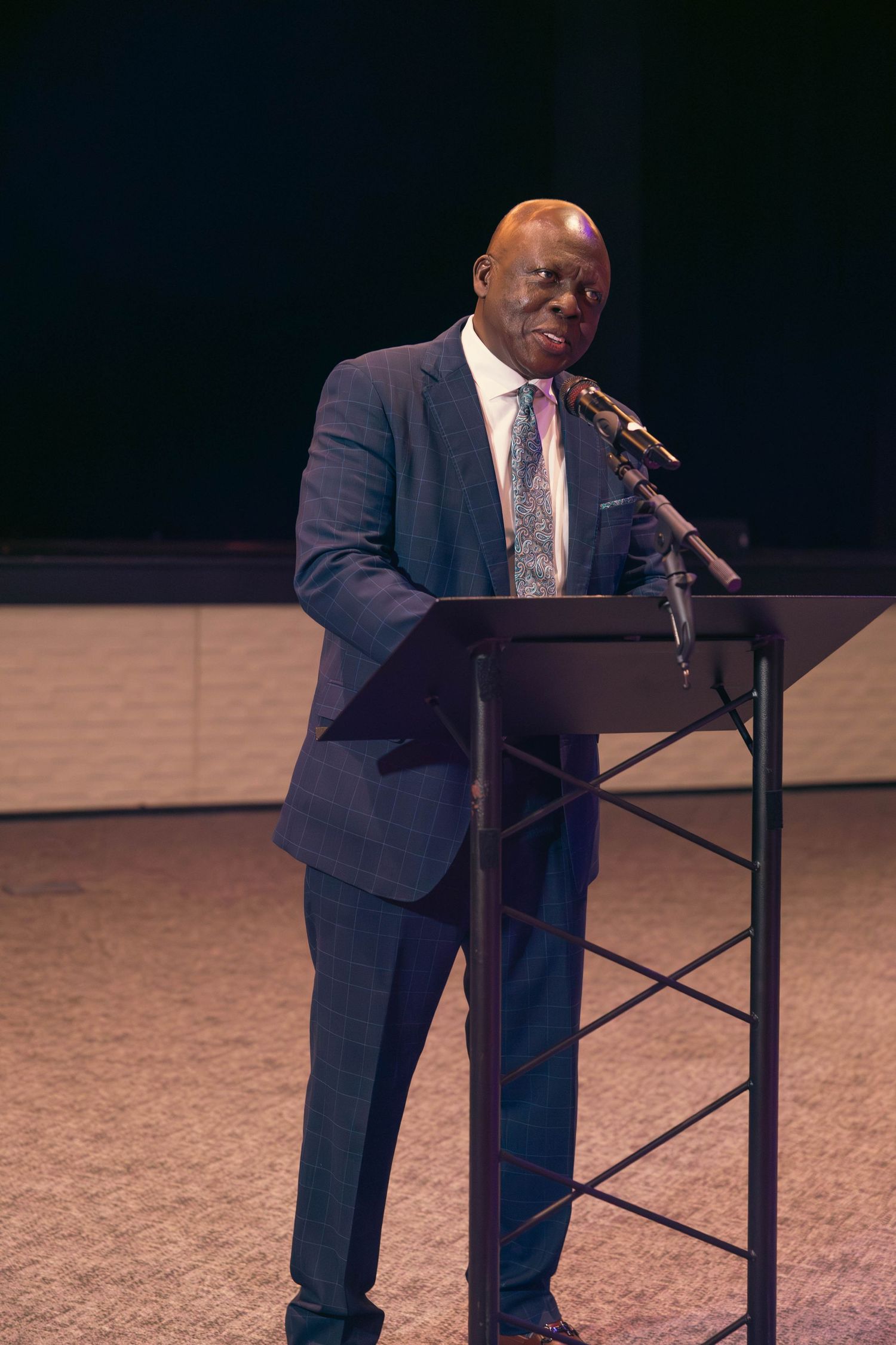 Man in blue suit delivers speech at podium during formal ceremony.