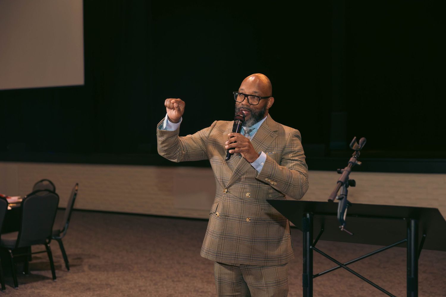Man in tan blazer gestures passionately while speaking at a formal event.
