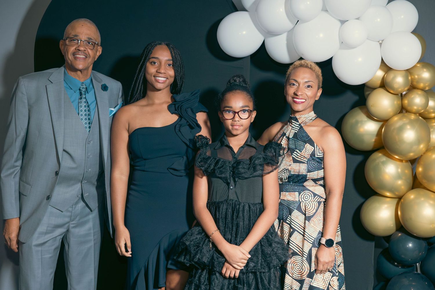 Family of four poses together at formal celebration with balloon backdrop.