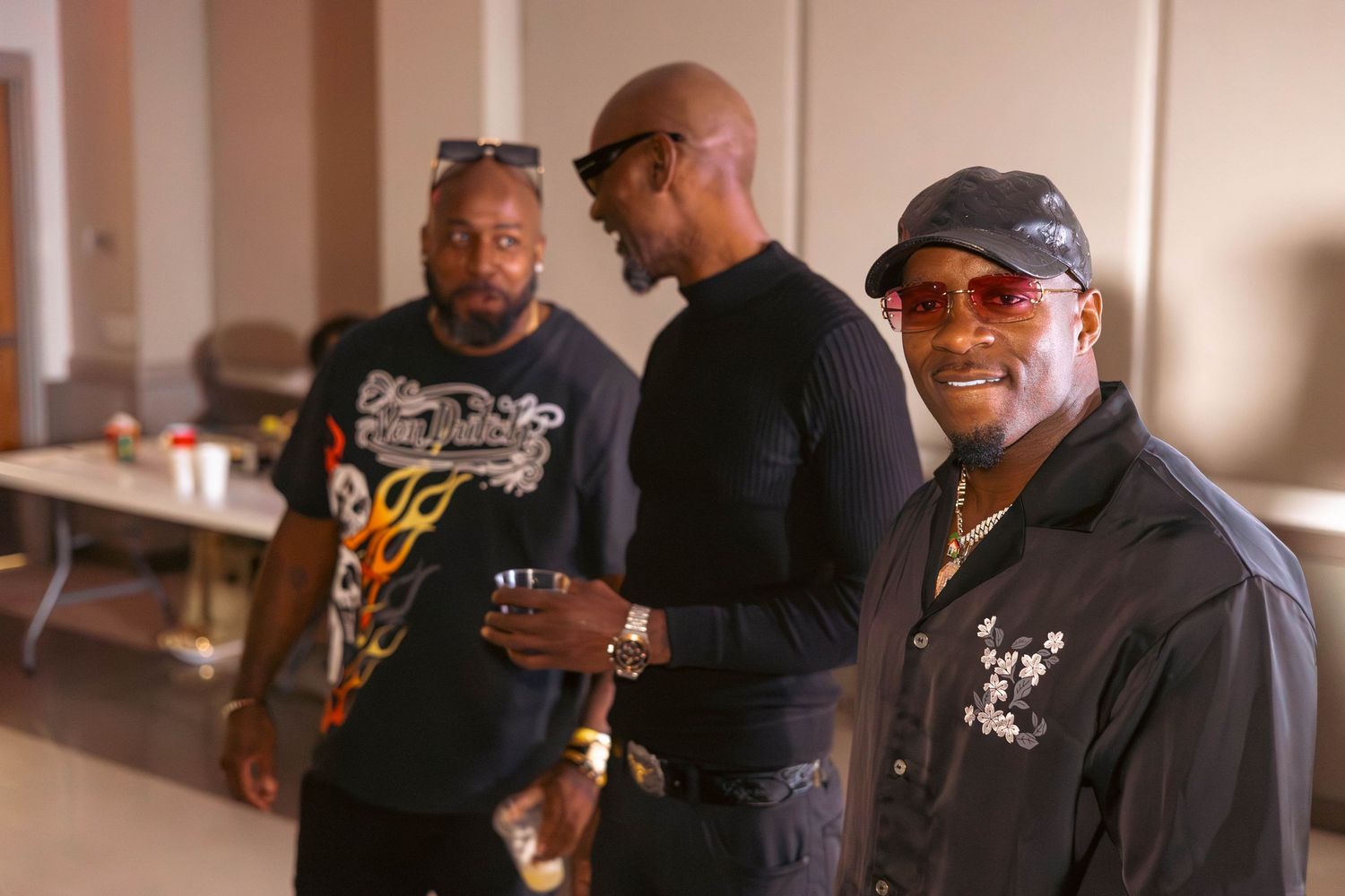 Three men in casual attire socializing and smiling at a reunion gathering.