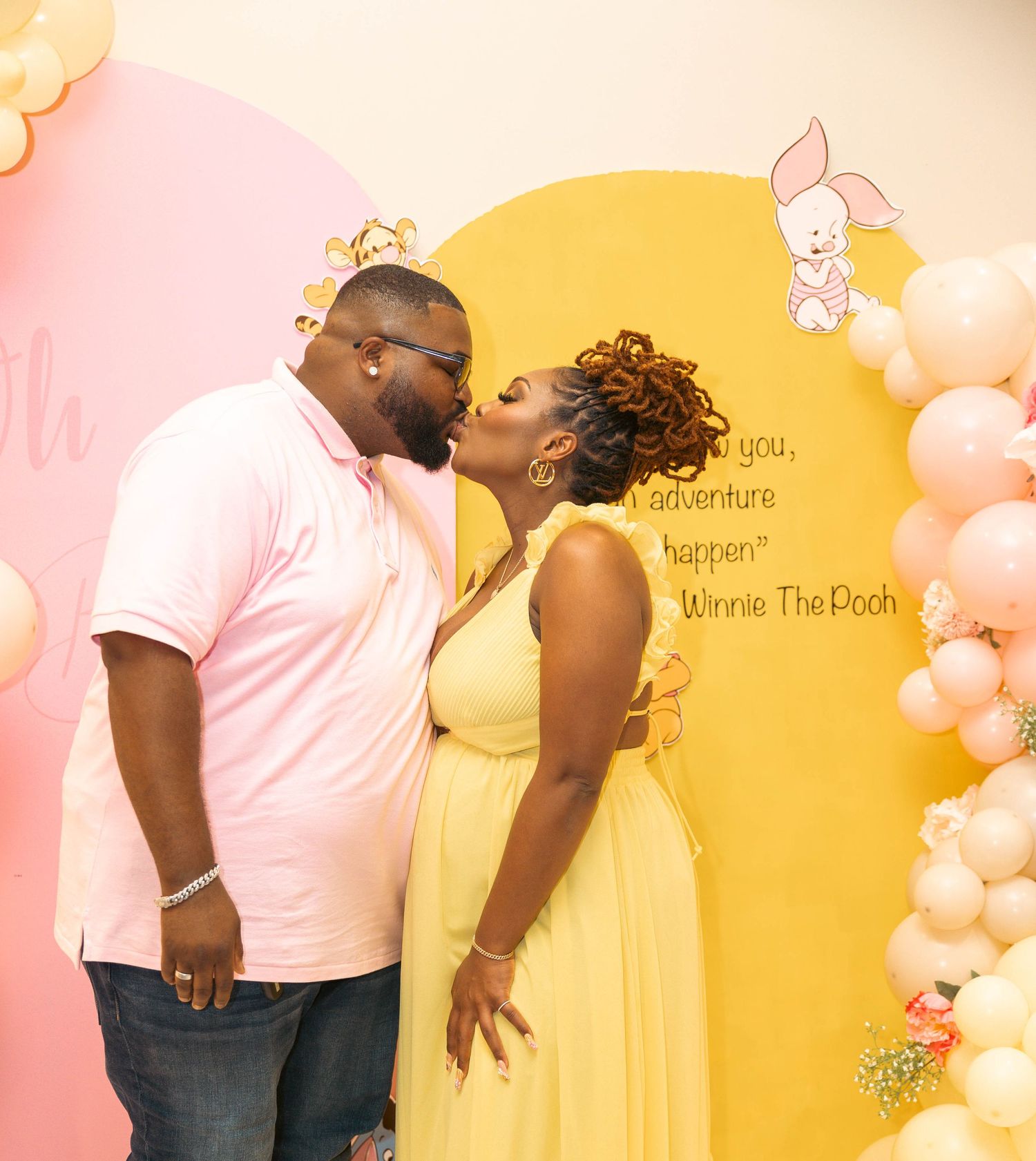 Couple kissing in front of Winnie the Pooh baby shower backdrop.