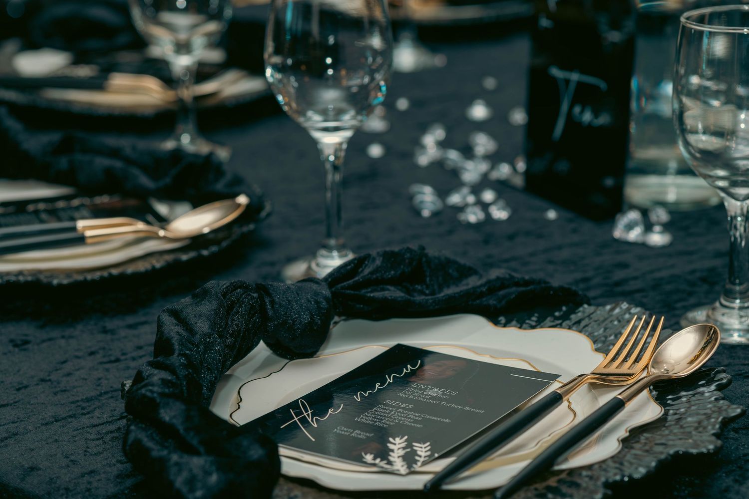 Sophisticated black velvet table setting with gold cutlery and elegant menu card at formal dinner.