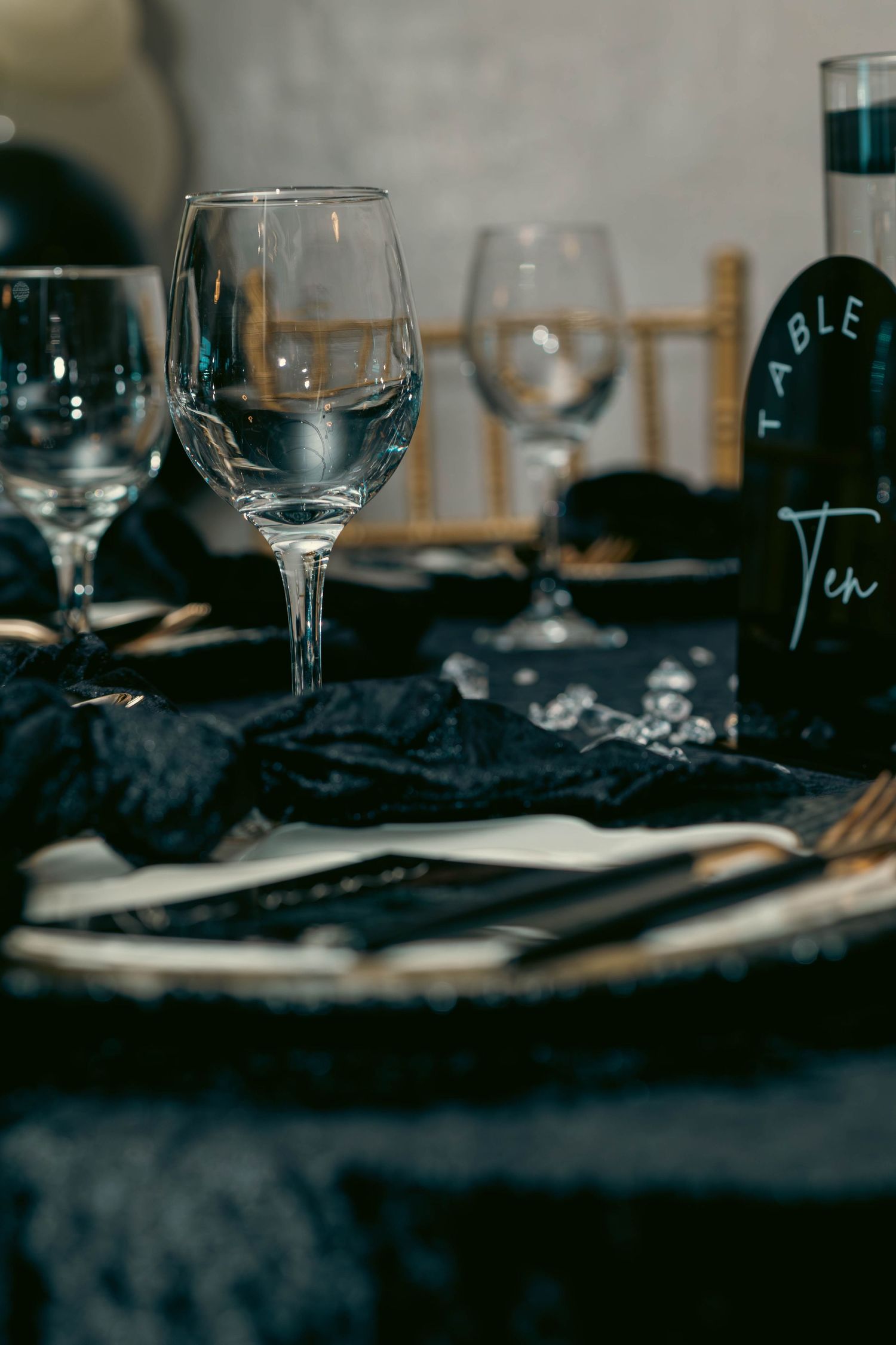 Elegant black and gold table setting with crystal wine glasses and Table Ten card at formal event.