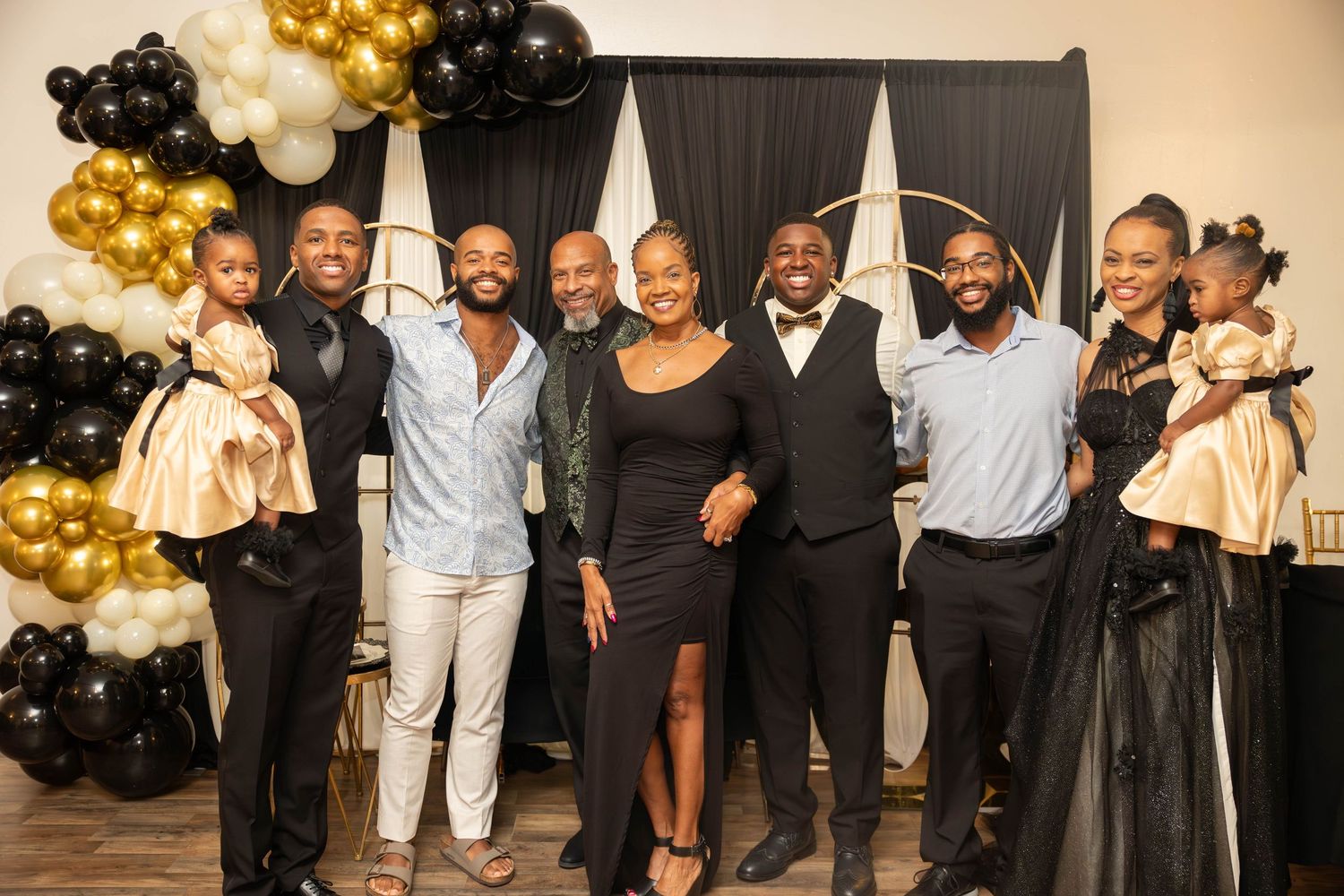 Group of elegantly dressed people posing together at a black and gold themed celebration party.