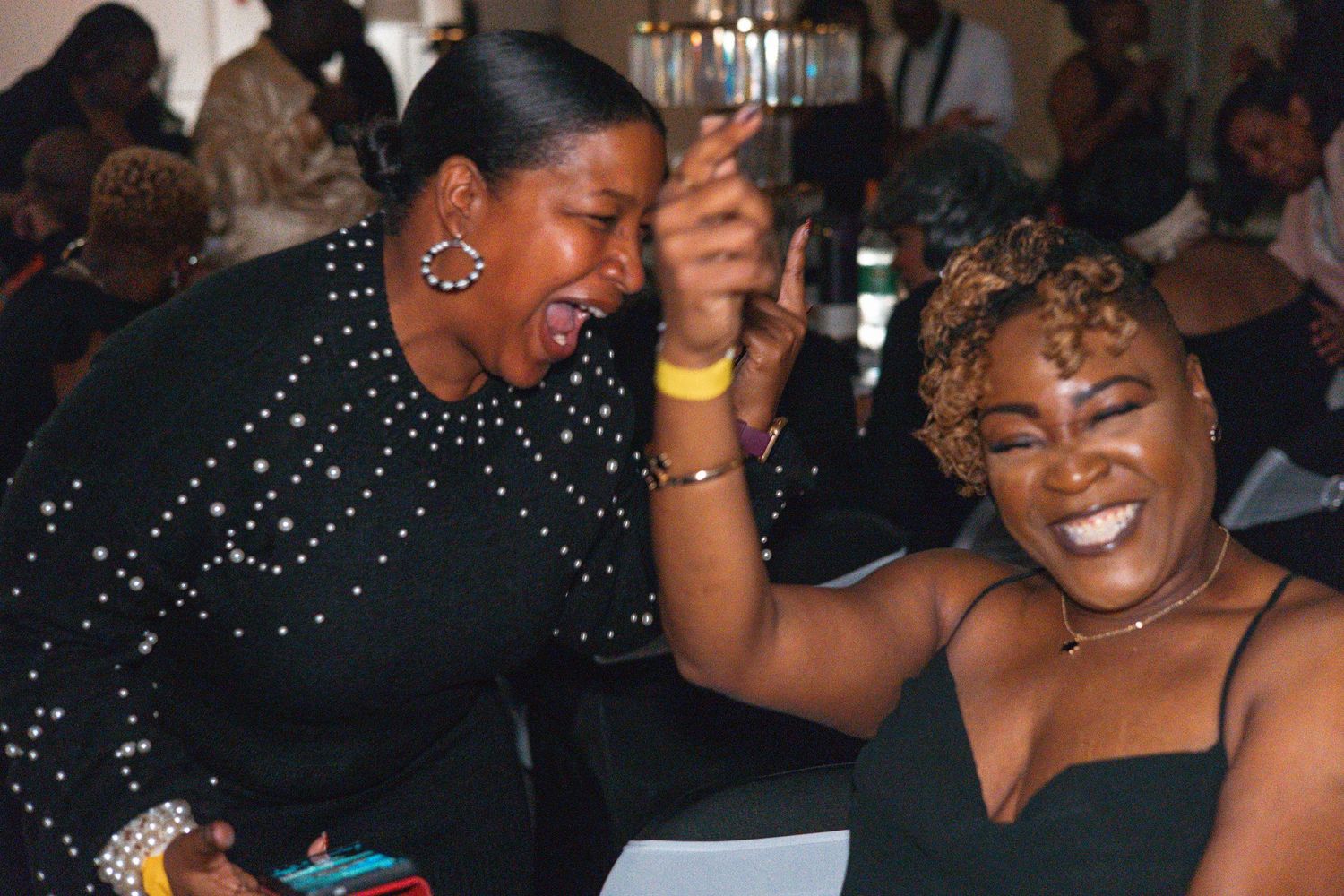 Two women laughing and celebrating joyfully together at a reunion dinner event.