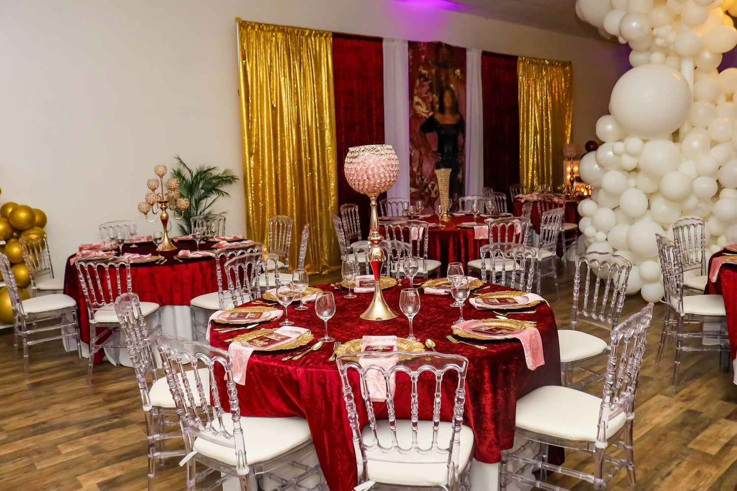 Elegant event venue with crimson velvet tablecloths, crystal centerpieces, and gold balloon arch decor.