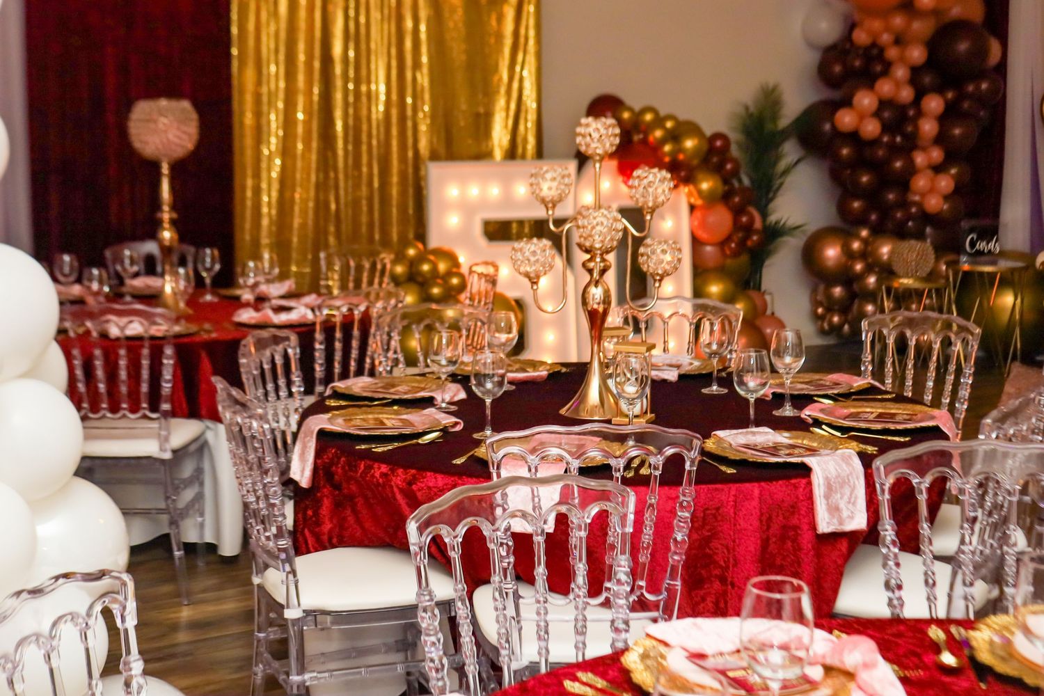 Luxurious banquet table with red velvet linens, crystal candelabra, gold chargers, and balloon decor.