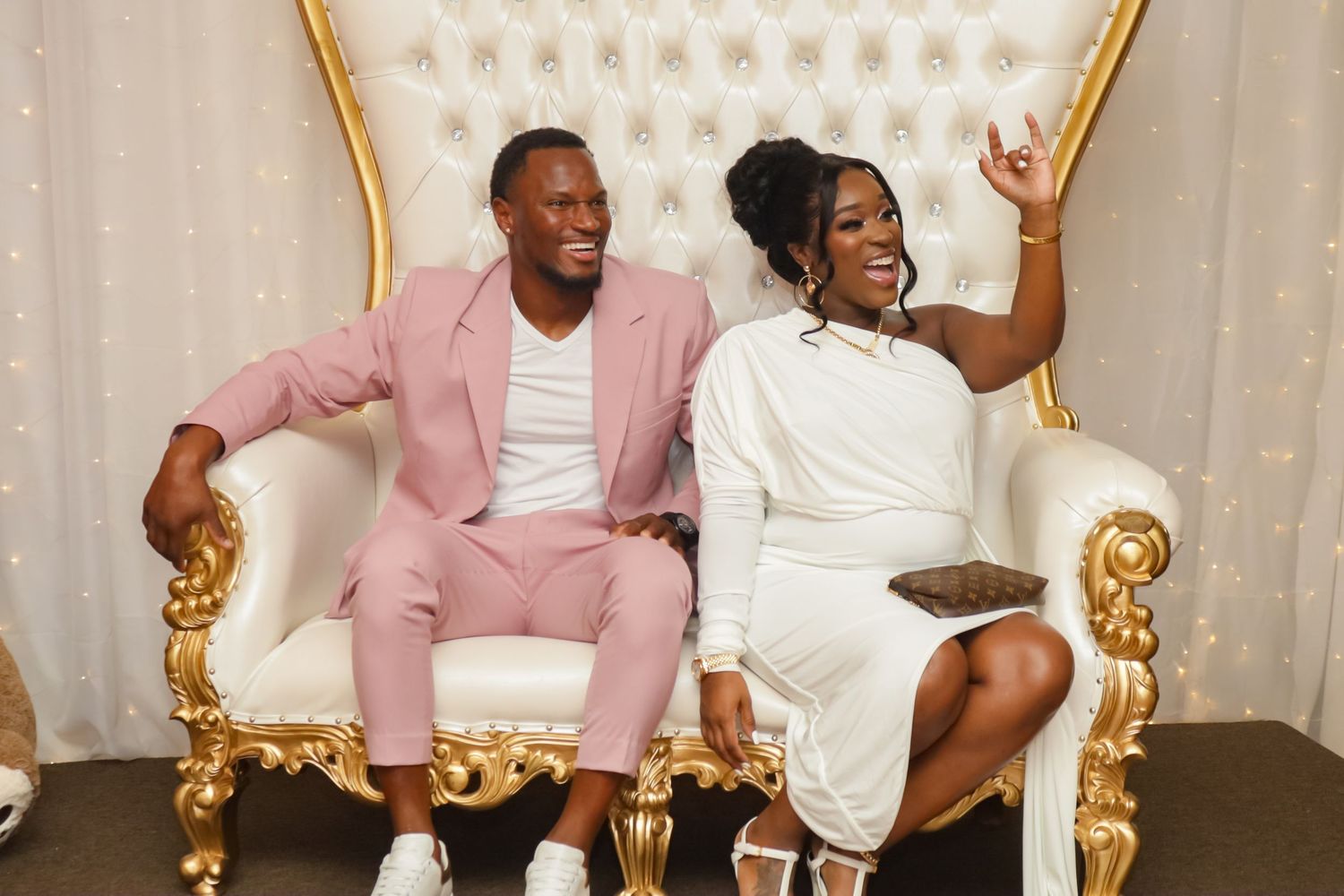 Couple sitting on ornate gold and white throne chair at elegant baby shower event.