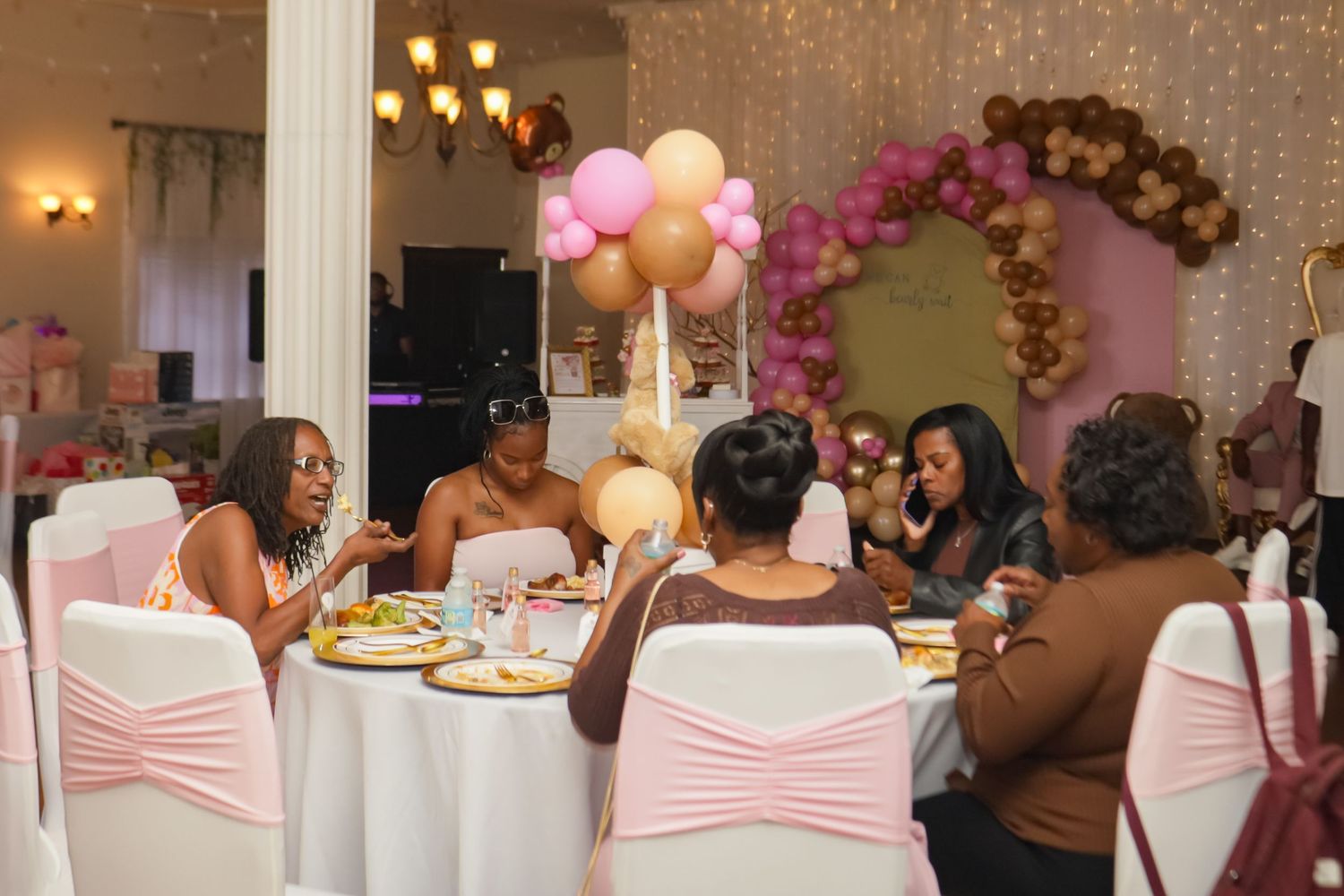 Women celebrate at a festive party with pink and gold balloon decorations and elegant table settings.