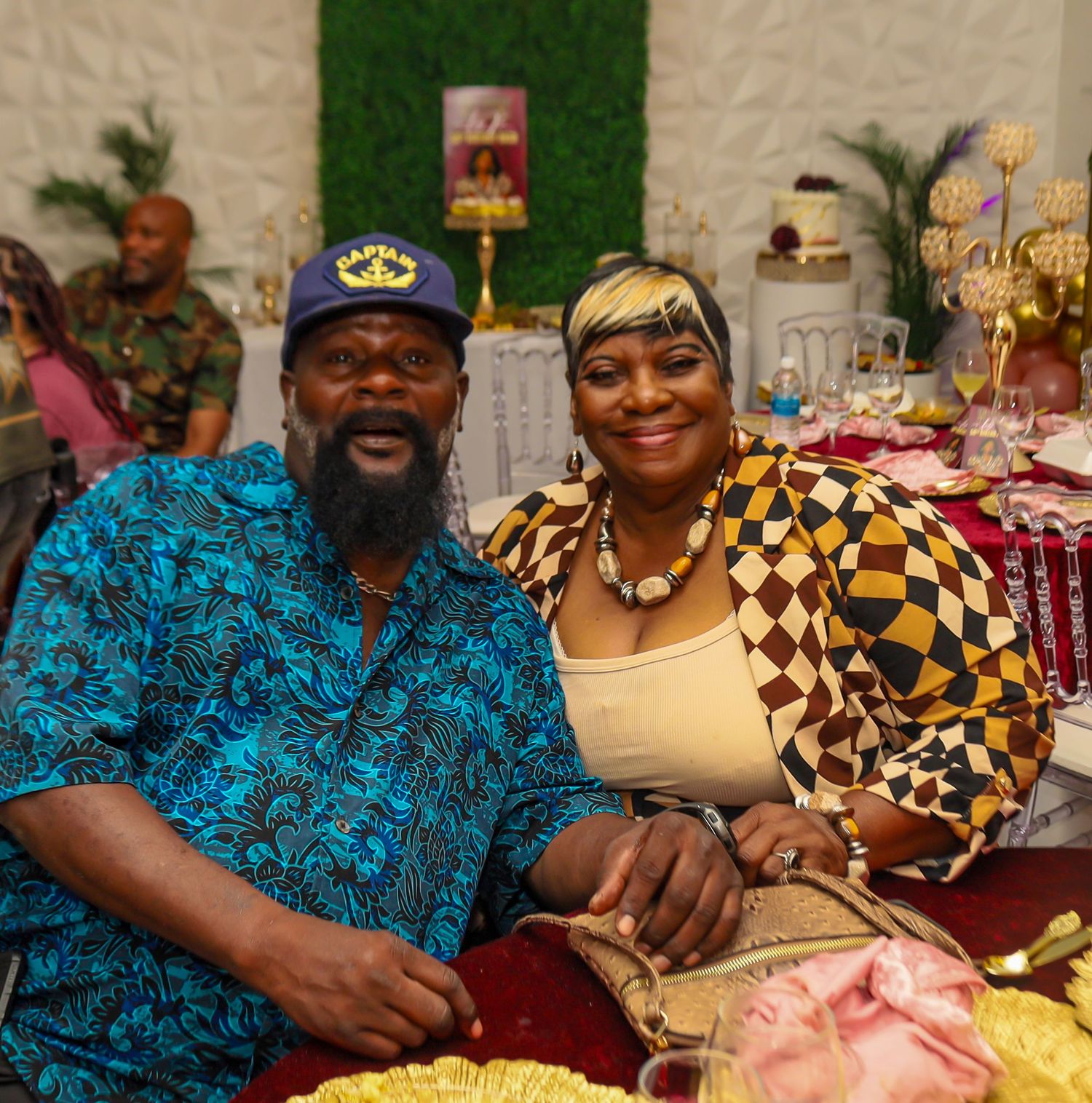 Couple in colorful African-print outfits smiling together at a festive celebration event.