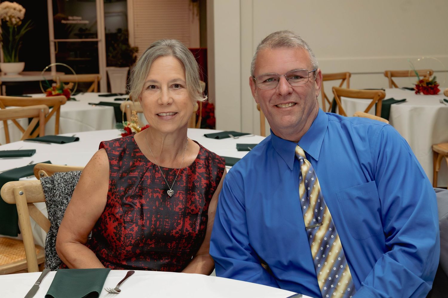 Smiling couple poses together at elegantly set dining tables during a formal banquet event.