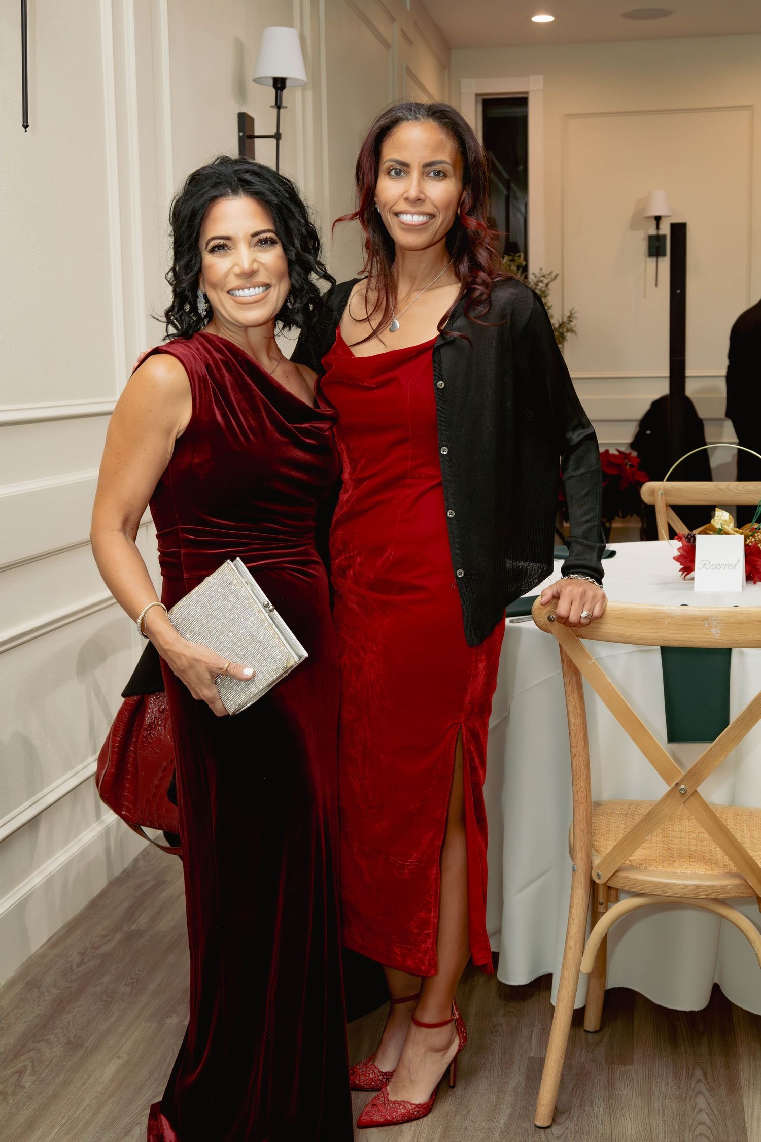 Two women in red dresses pose together at an elegant holiday dinner party event.