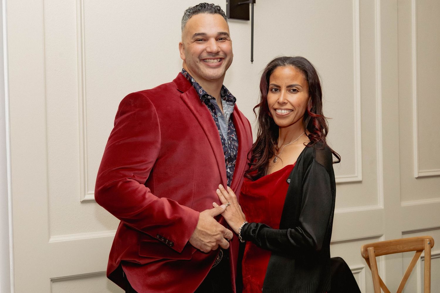Couple posing together at formal event, man in red velvet blazer and woman in red dress.