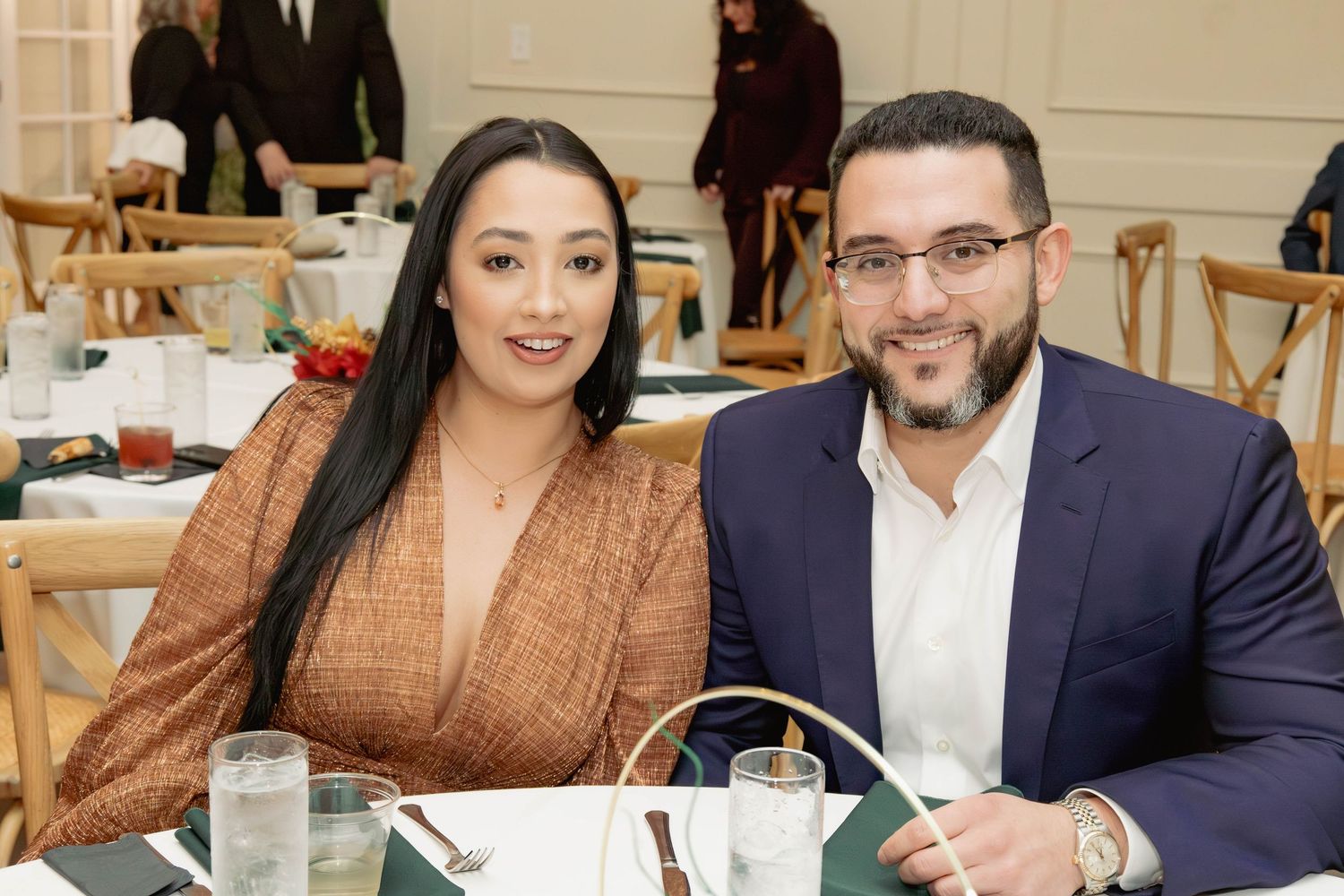 Couple smiling together at formal dinner event, woman in brown dress and man in blue suit.