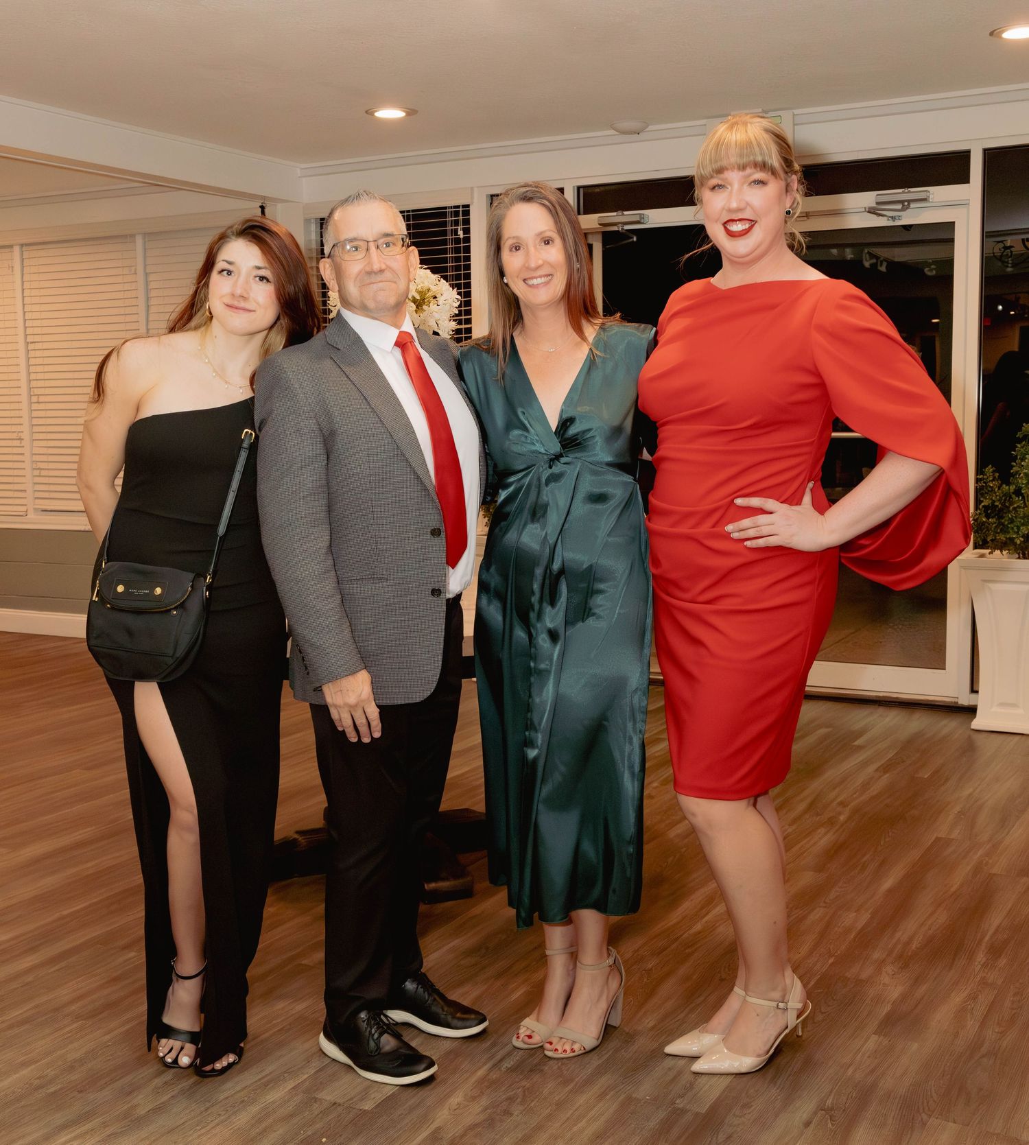Group of four people in formal attire pose together at an elegant holiday dinner event.