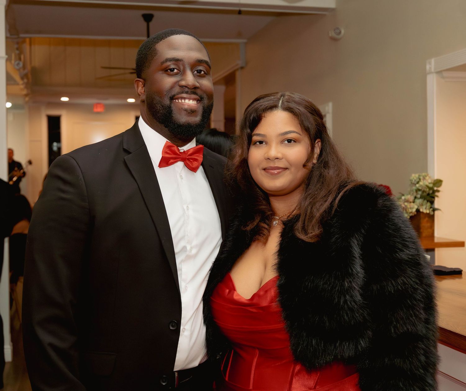 Couple in formal red and black attire smiles together at an elegant evening gala event.