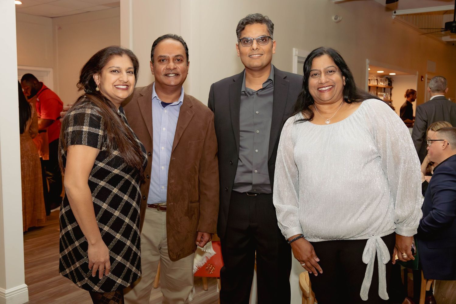 Group of four people smiling together at a social gathering in a bright indoor venue.