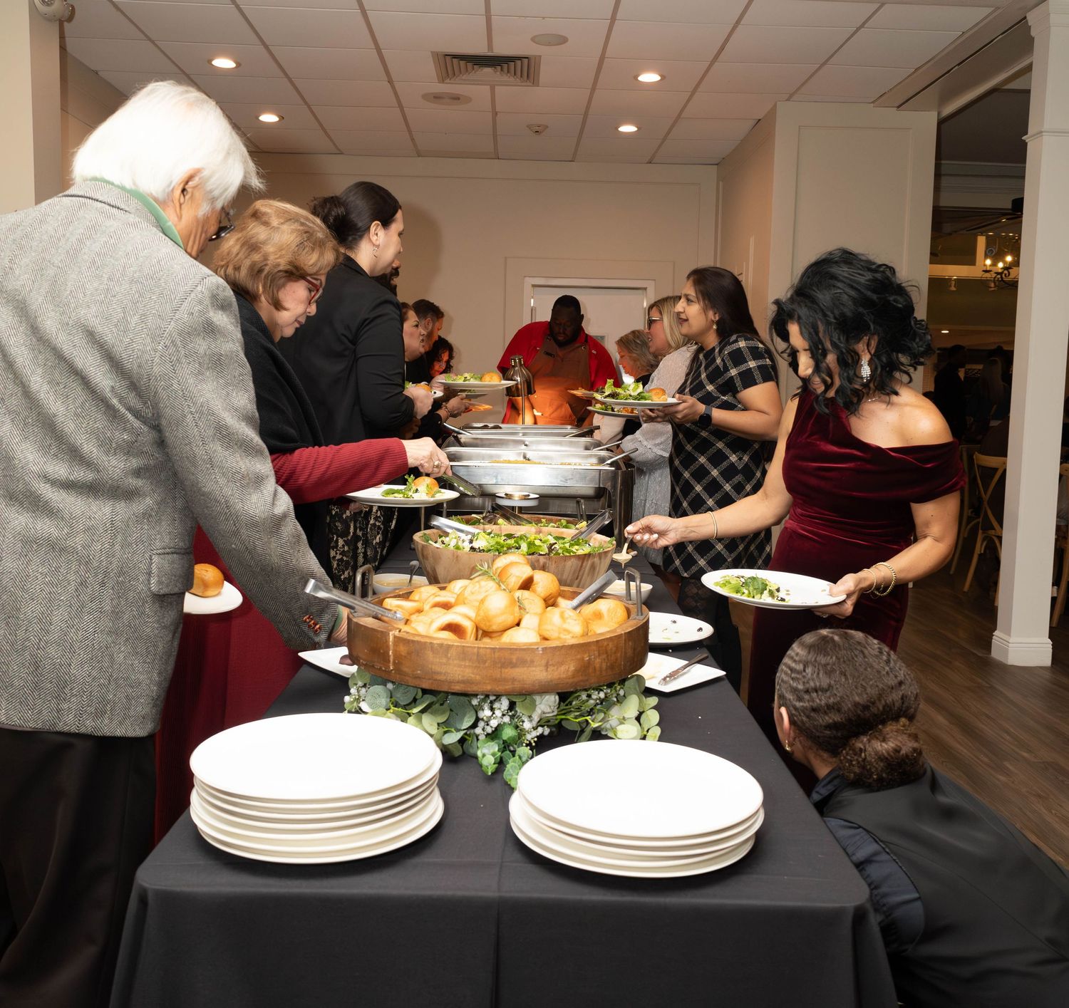 Guests serving themselves at a buffet table with white plates and various food dishes at an event.