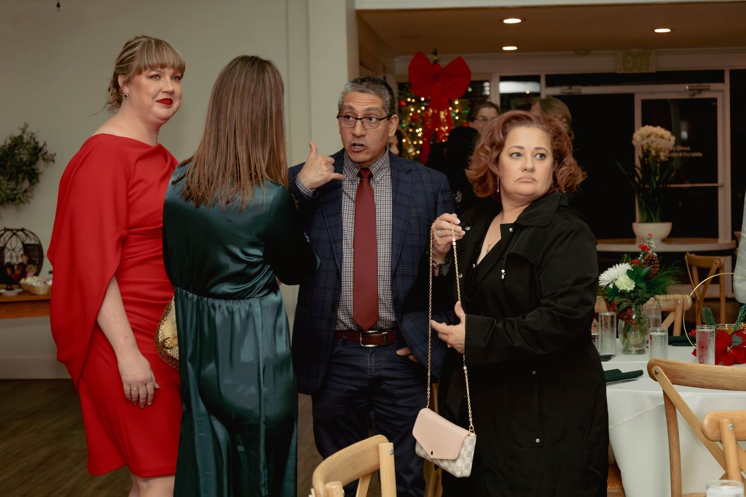 Four people conversing near a Christmas tree at a holiday party in an elegant venue.