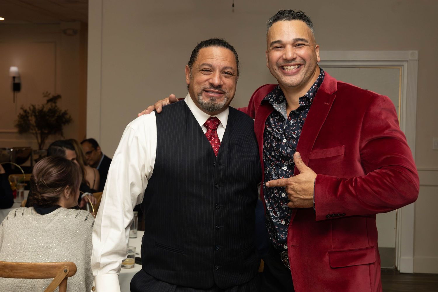 Two men posing together at formal event, one in burgundy velvet blazer and one in vest.