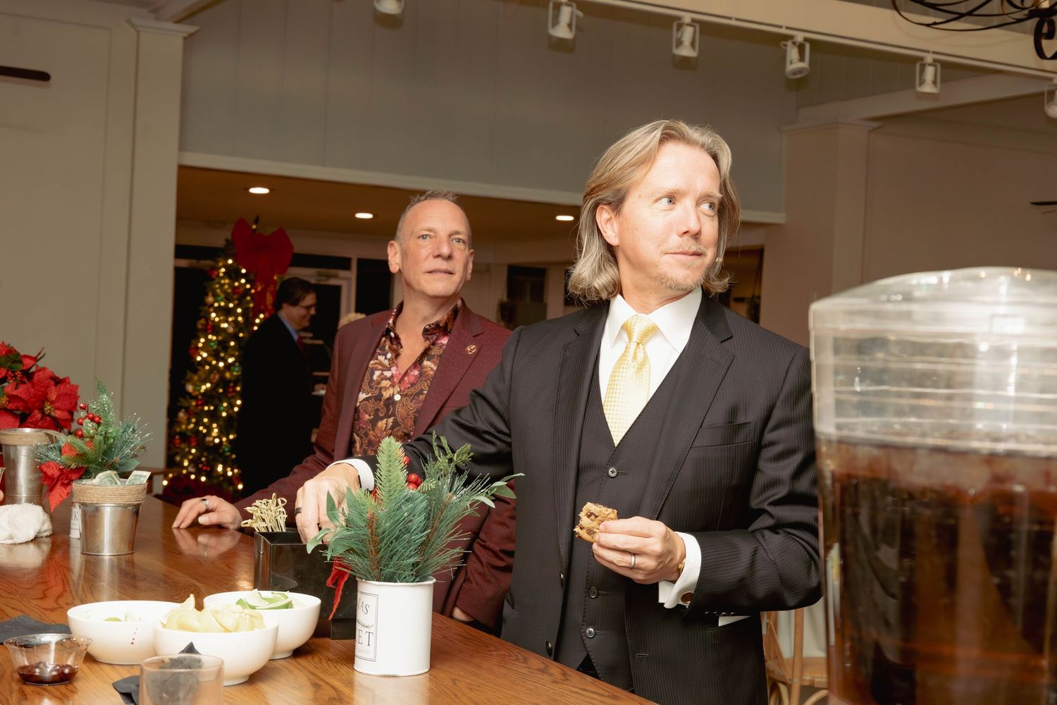 Two men standing near a refreshment table with Christmas decorations at a holiday gathering.