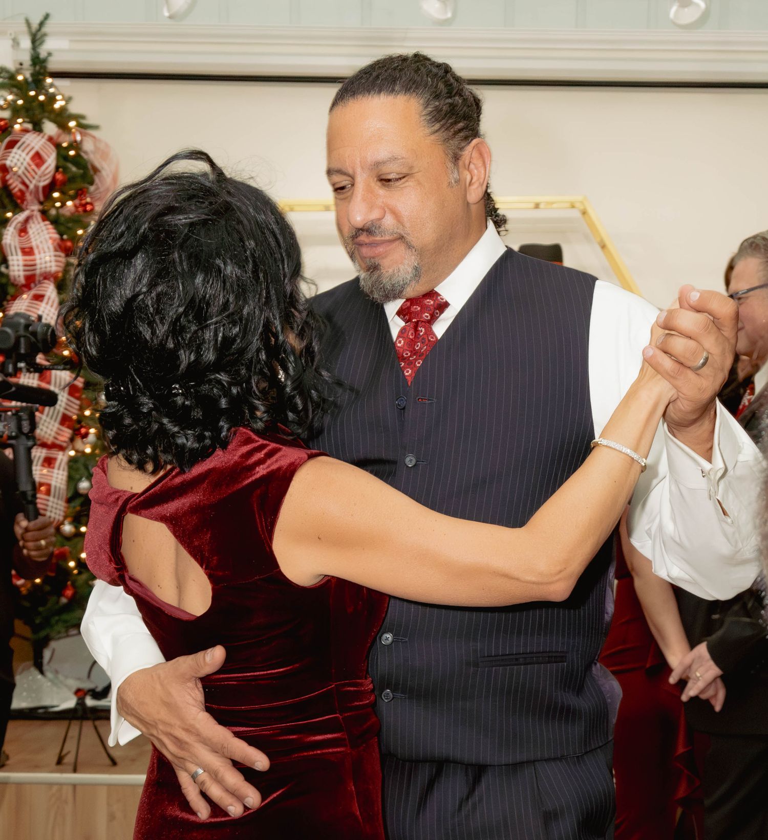 Couple dancing closely together at a holiday party near a decorated Christmas tree.