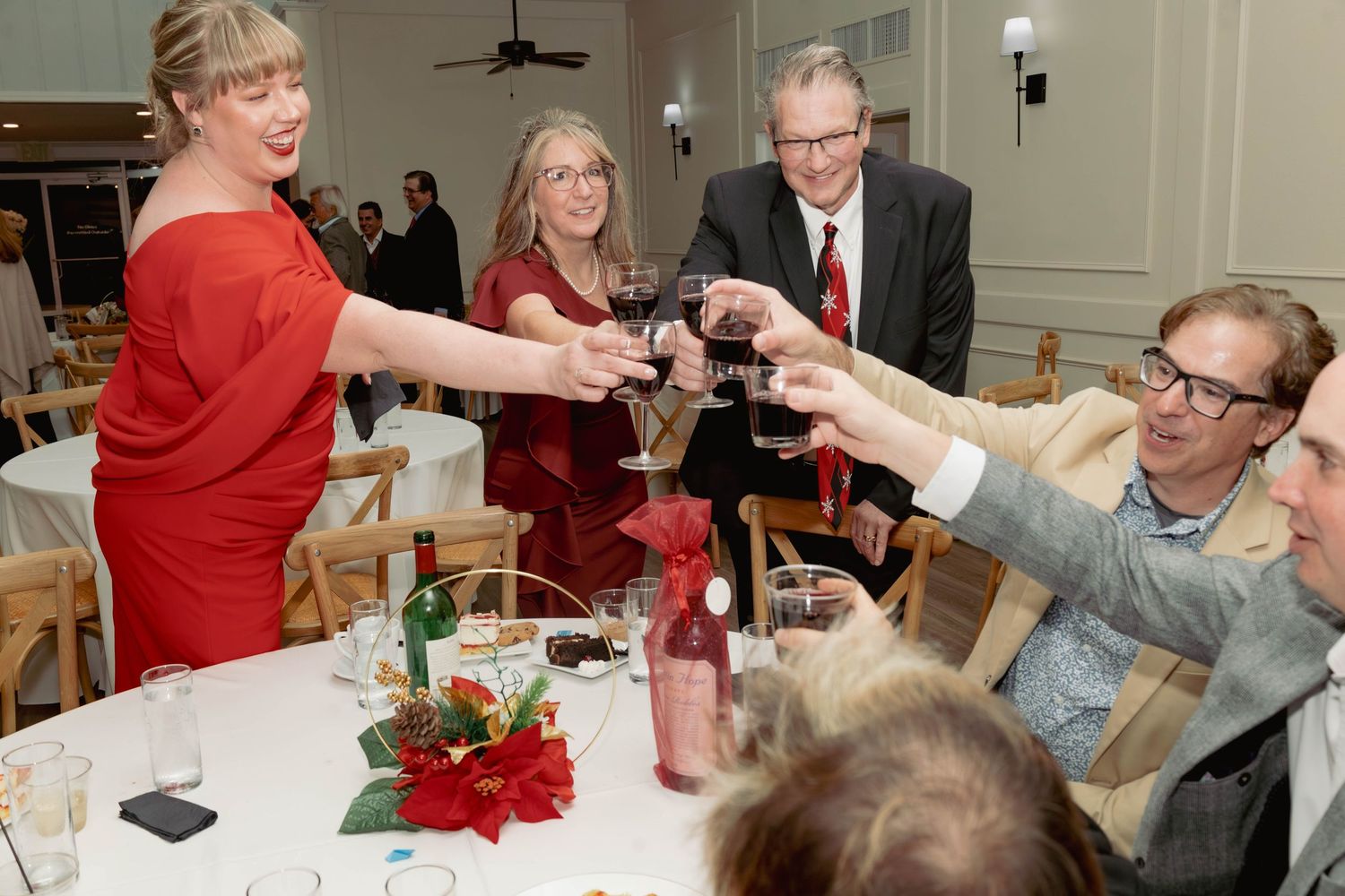 Group of guests raising wine glasses in a toast at a festive holiday dinner party.