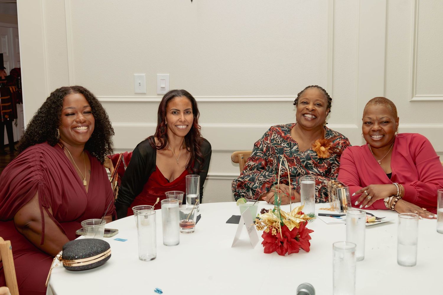 Four women smiling together at a round table during a festive holiday celebration event.