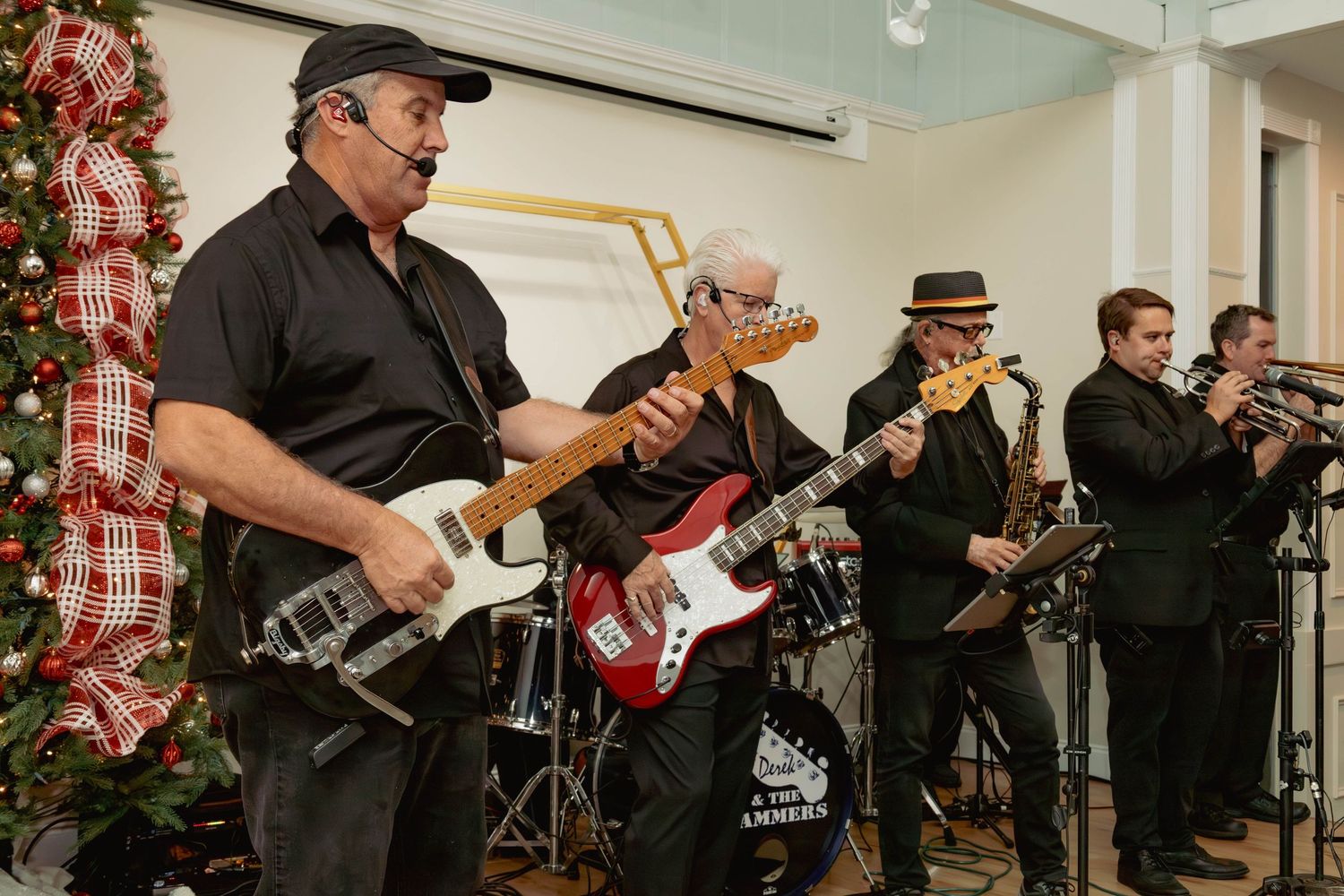 Live band performing holiday music featuring guitar, bass, saxophone, and trumpet players at a Christmas event.