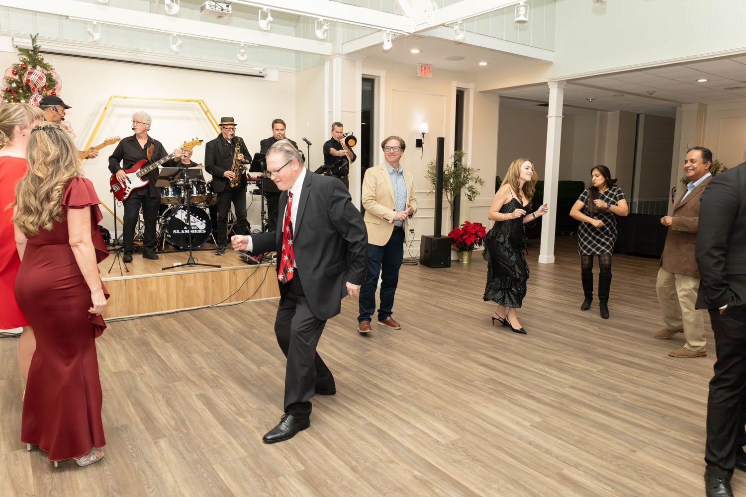 Guests dancing and socializing at a festive holiday party with a live band performing in the background.