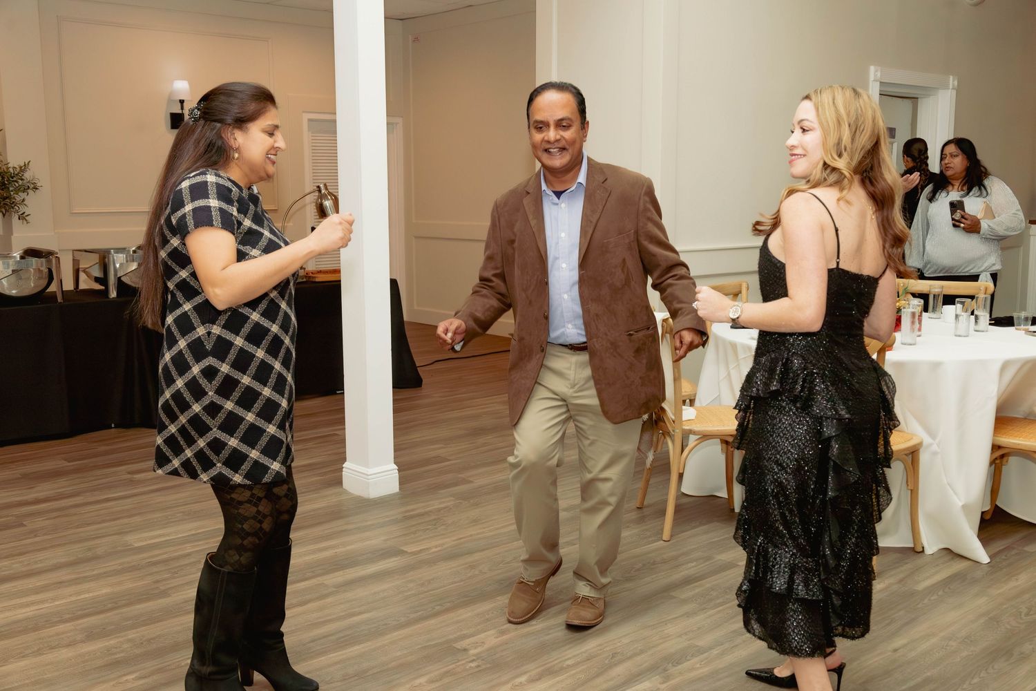 Three guests dancing and socializing at an elegant indoor event venue with white columns and hardwood floors.