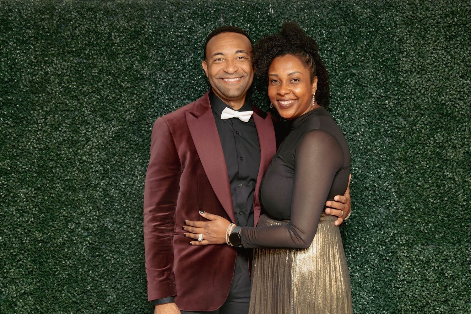 Couple posing together in formal attire in front of a lush green hedge photo backdrop wall.