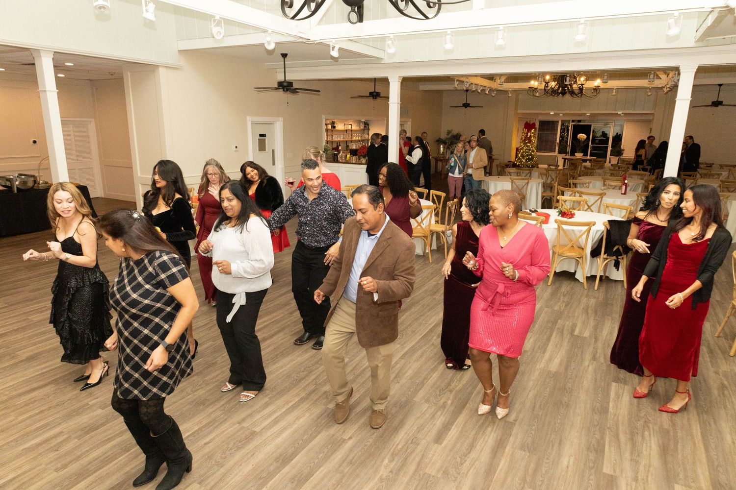 Diverse group of elegantly dressed guests dancing together on a dance floor at a formal event.