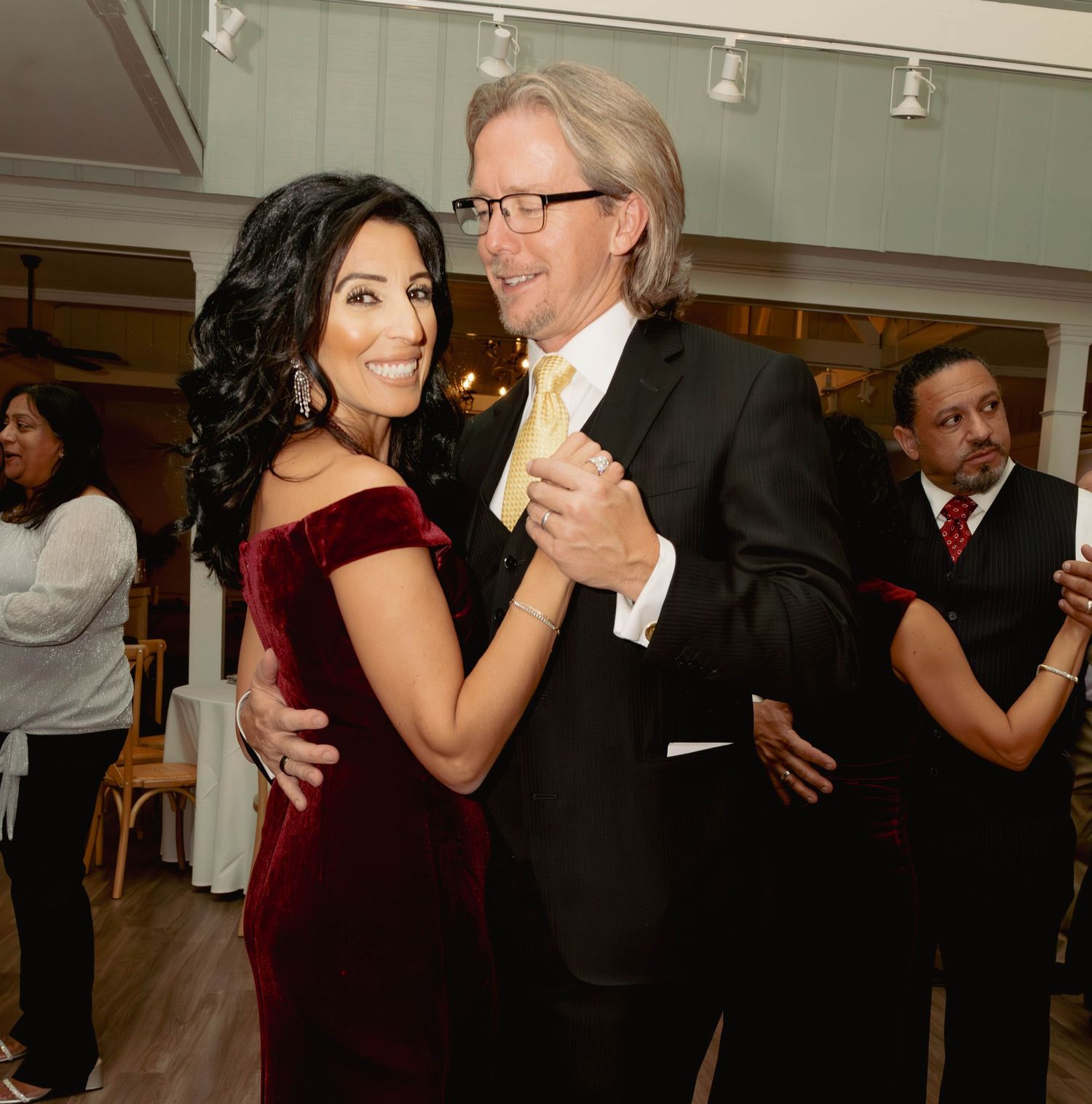 Couple sharing a romantic dance at a formal event, woman in red velvet dress with man in suit.
