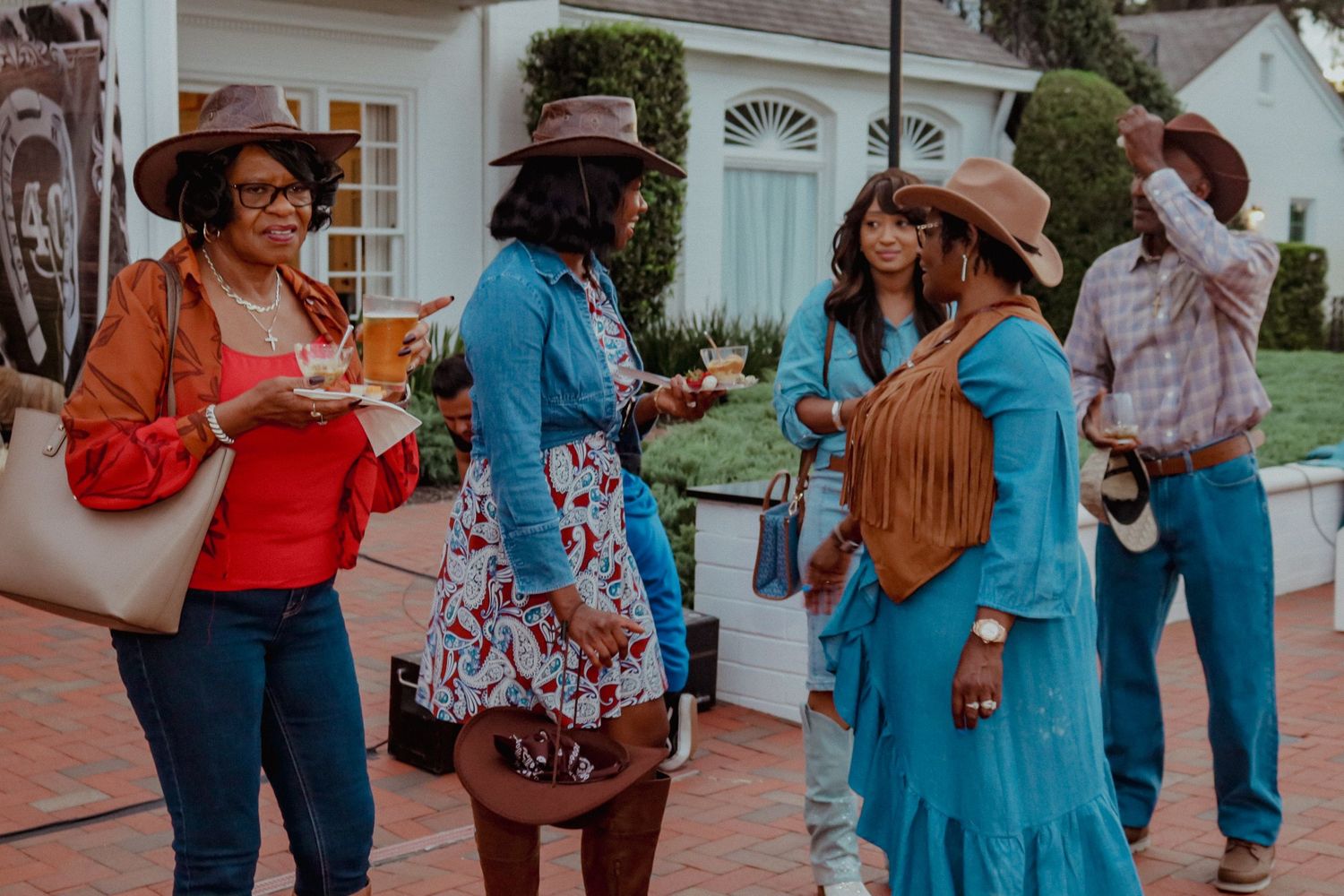 Group of guests in western-themed outfits socializing outdoors at a party.
