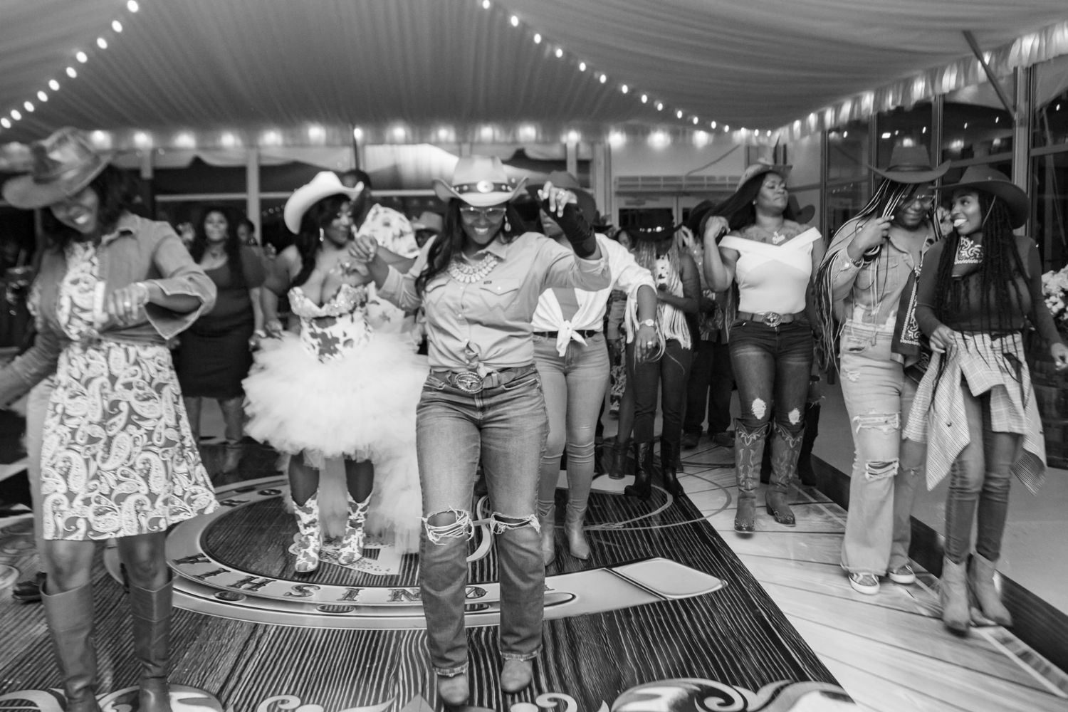 Black and white photo of guests line dancing at a western-themed birthday celebration.