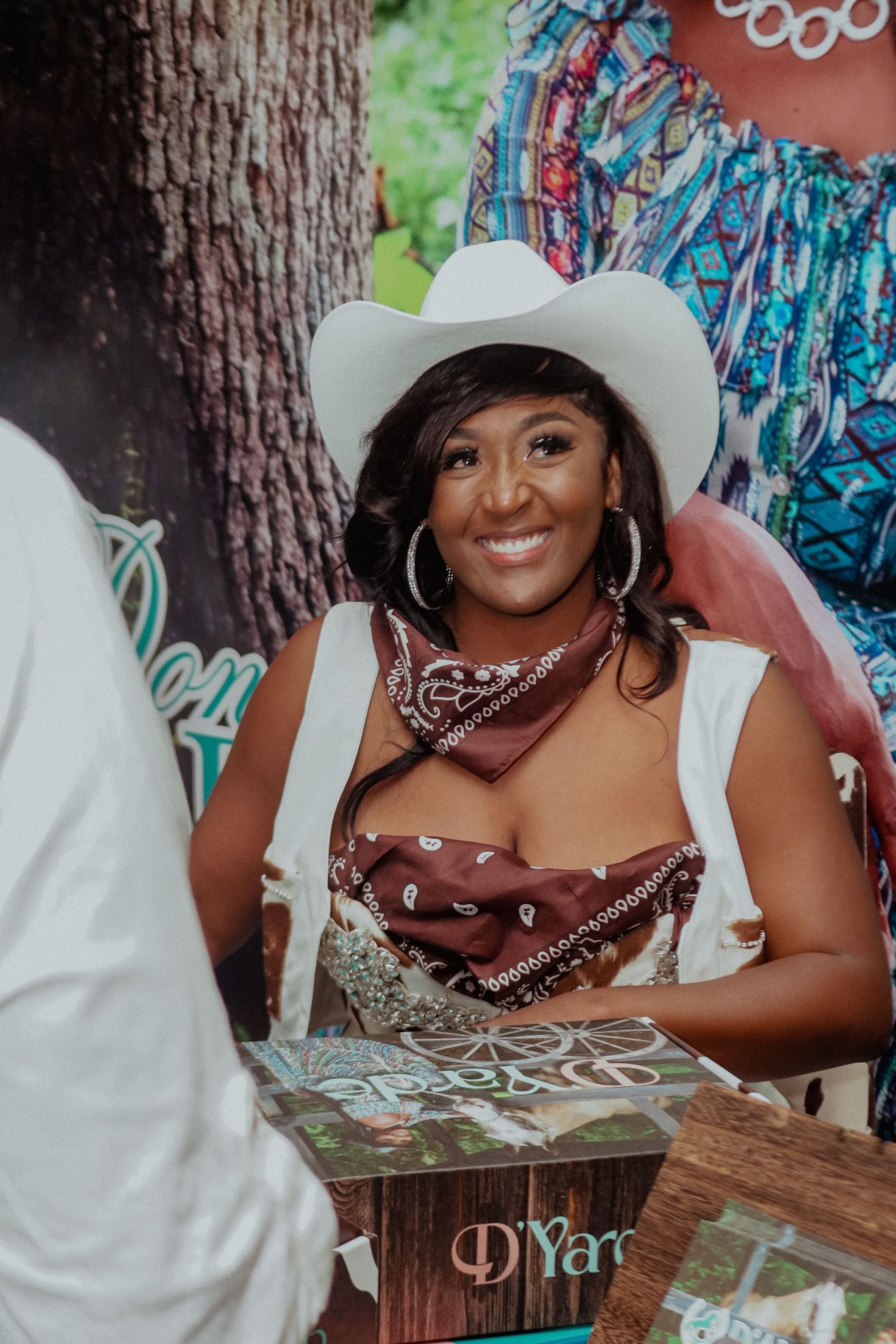 Smiling woman wearing white cowboy hat and brown bandana at Western-themed outdoor party event.
