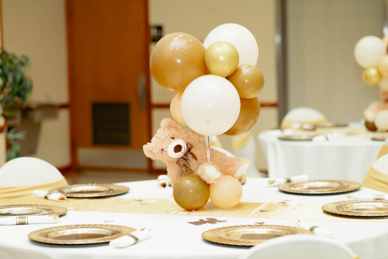 Elegant baby shower table centerpiece with gold and white balloons and a teddy bear.